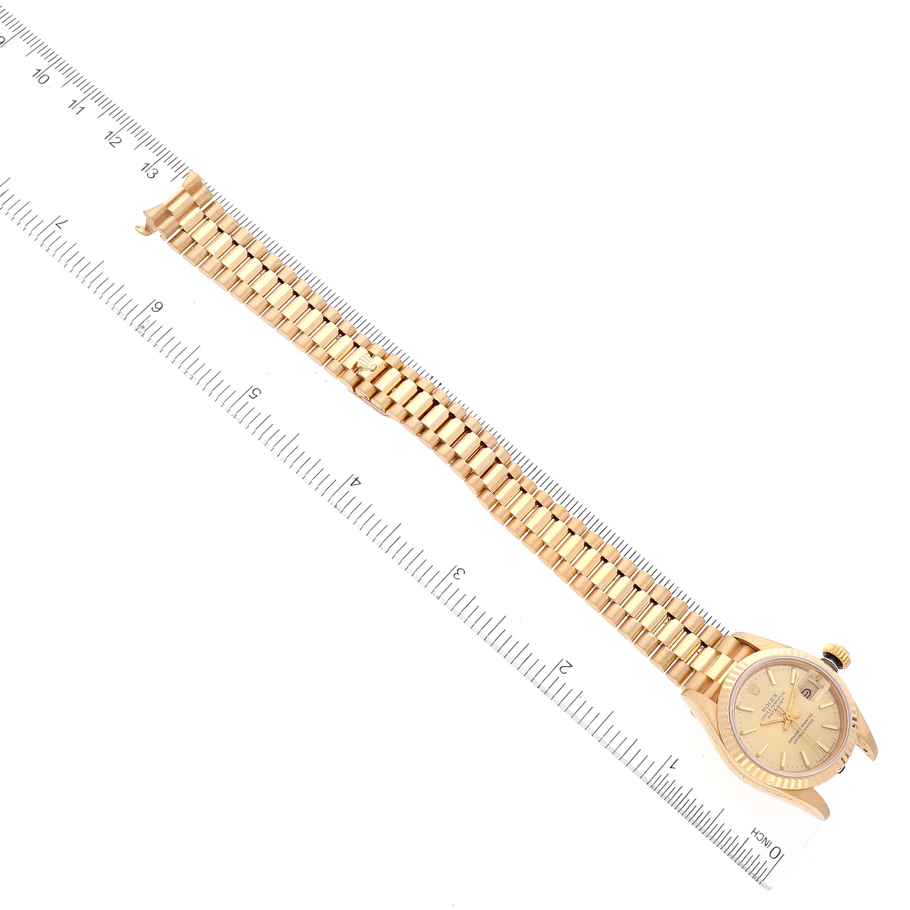 The image shows a Rolex President 69178 Women
s Yellow Gold Champagne Dial 69178 Women
s Yellow Gold Champagne Dial model watch laying flat, positioned next to a ruler for size reference.
