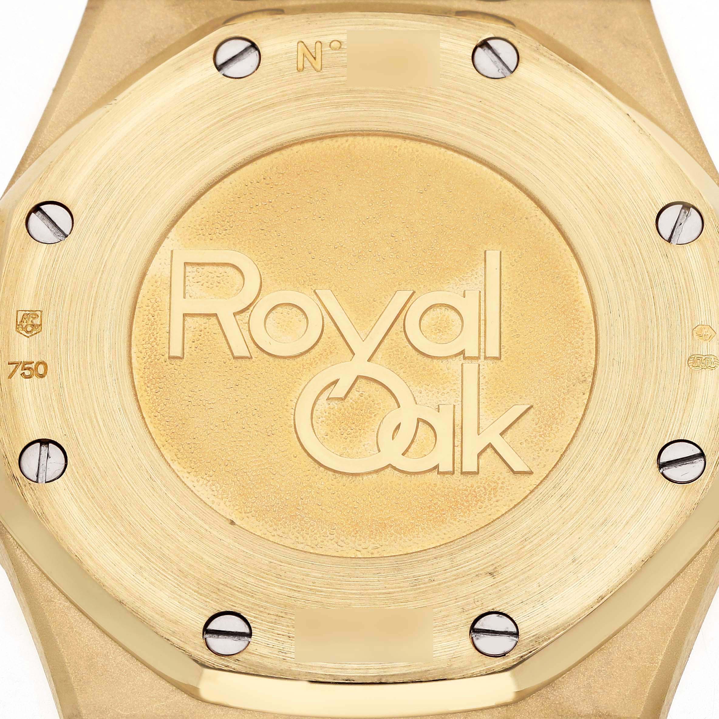 The image shows the gold case back of an Audemars Piguet Royal Oak 26120BA Men's Yellow Gold Silver Dial, featuring the model's engraved logo and screws.
