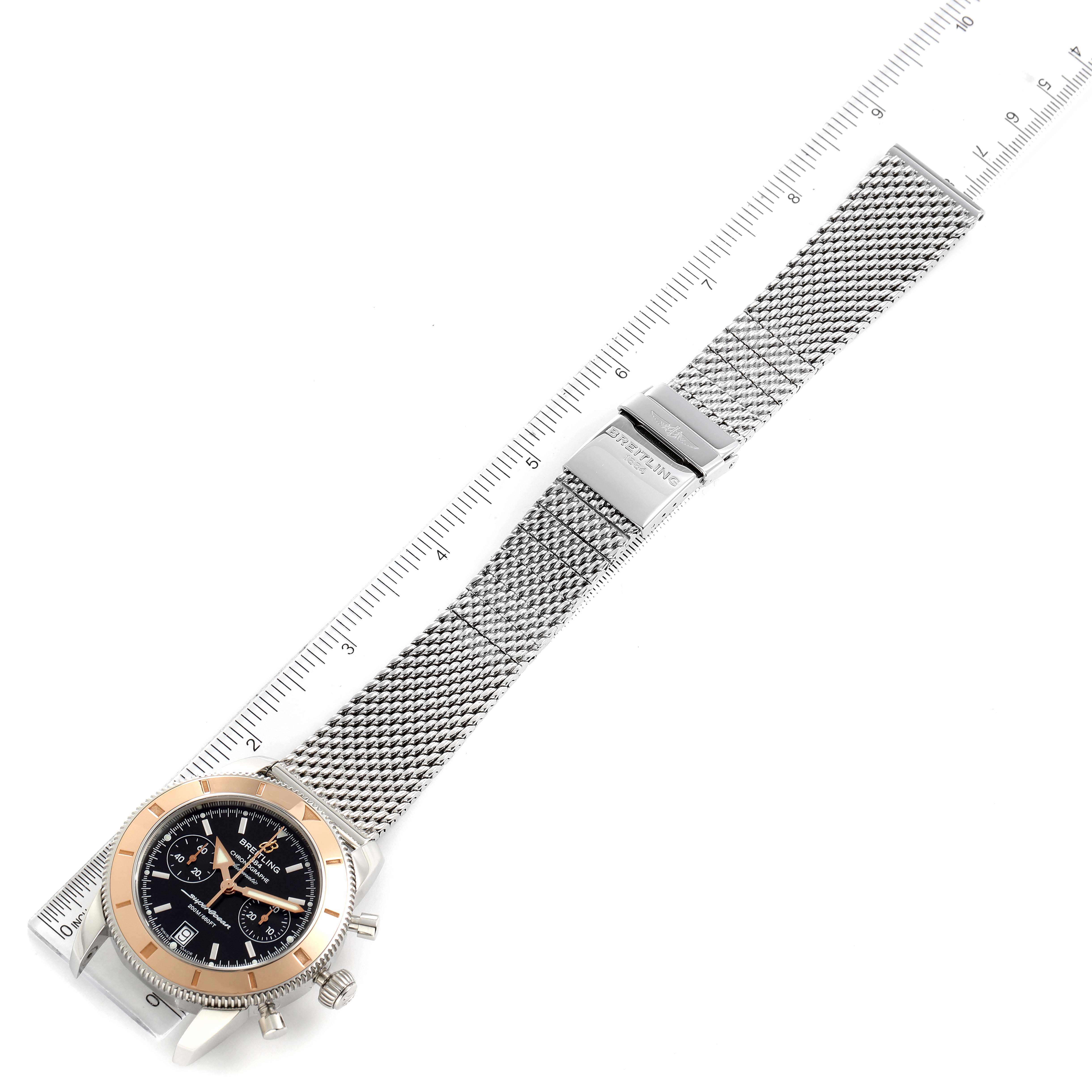 The image shows the Breitling Superocean U23370 Men
s Steel and Gold (two tone) Black Dial U23370 Men
s Steel and Gold (two tone) Black Dial watch laid flat with its metal mesh band extended and a ruler for scale.