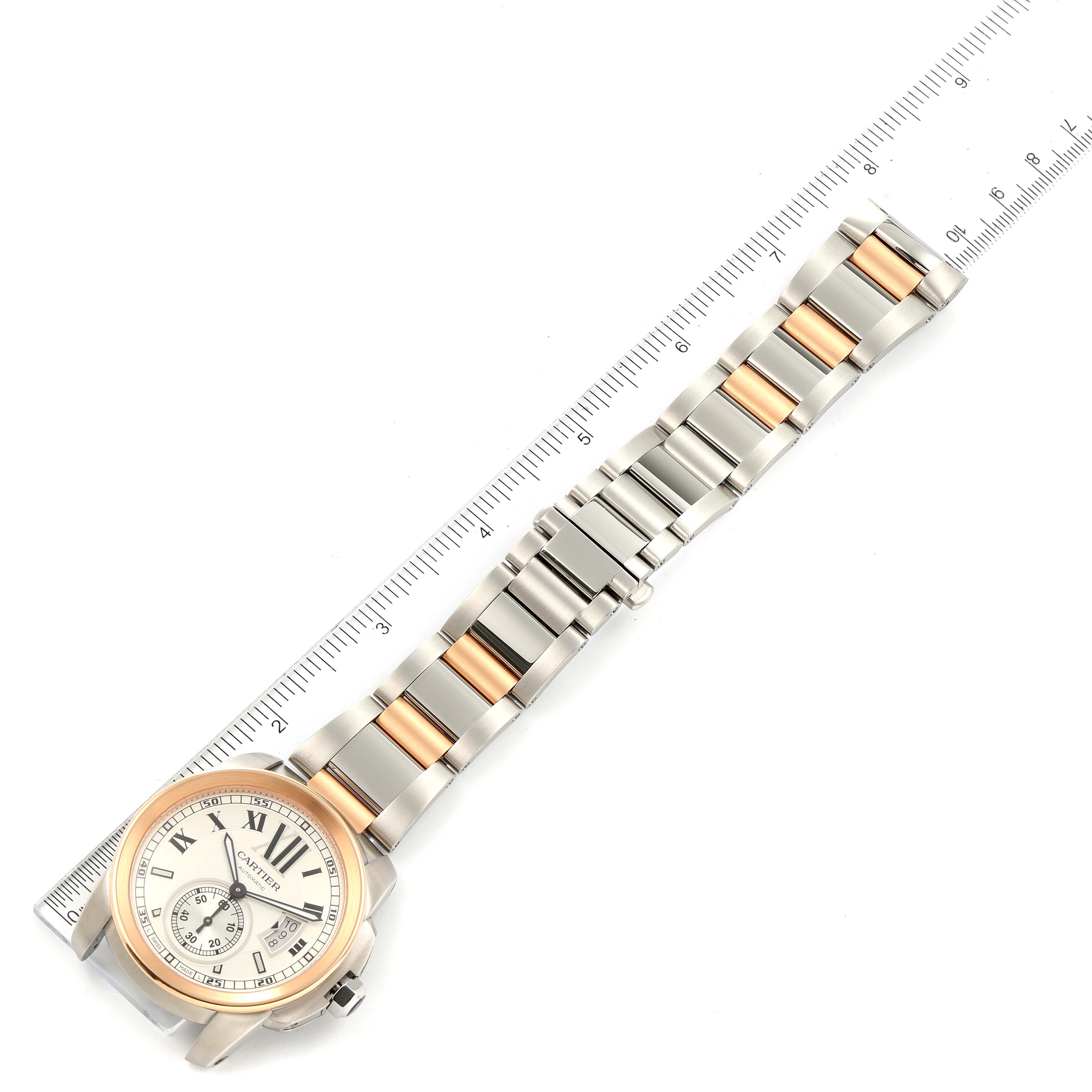 The image shows a top view of the Calibre de Cartier watch by Cartier, displaying its face, band, and a ruler for scale.