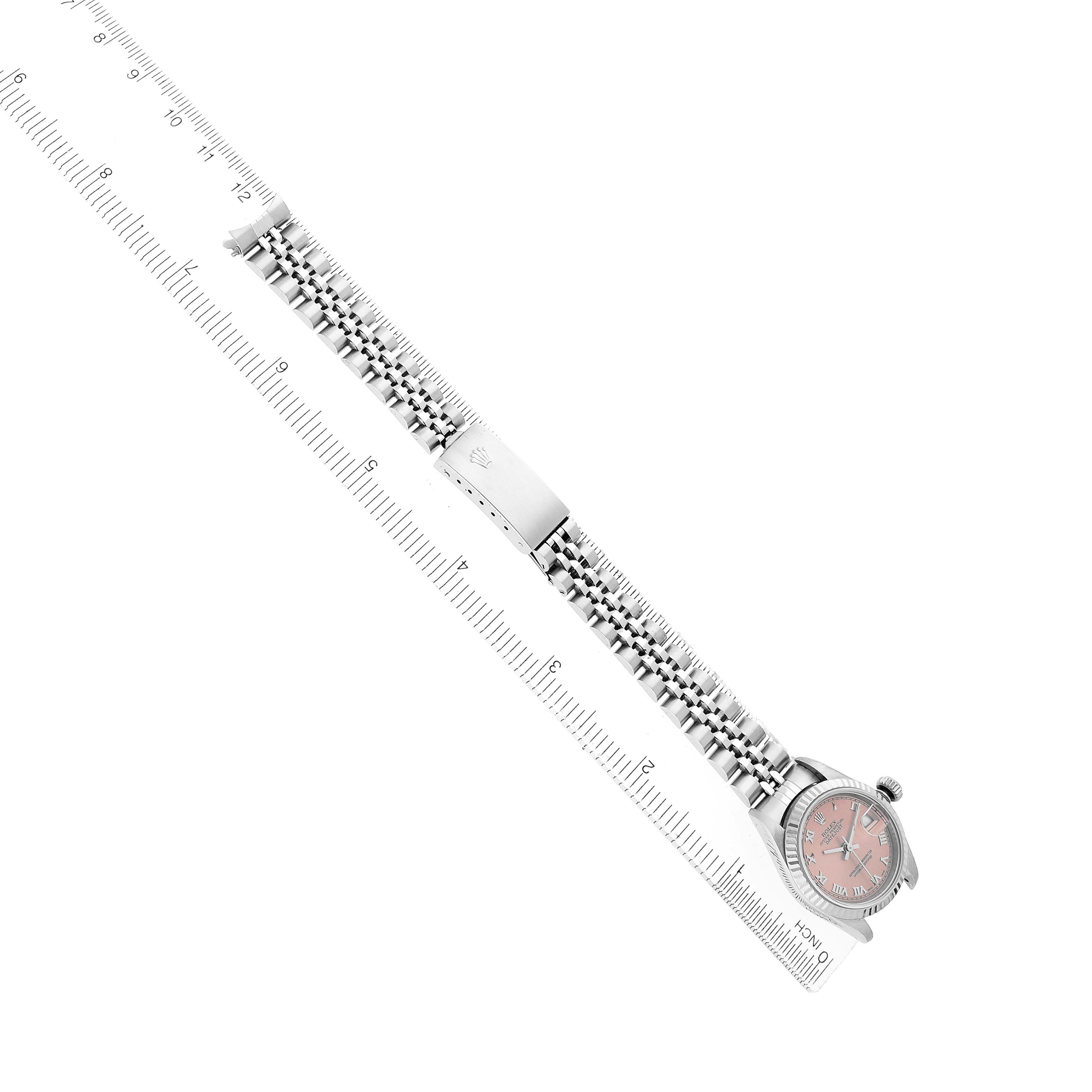 The Rolex Datejust 79174 Women's Stainless Steel Pink Dial watch is shown from a top-down angle, displaying the bracelet, clasp, and part of the watch face alongside a ruler.