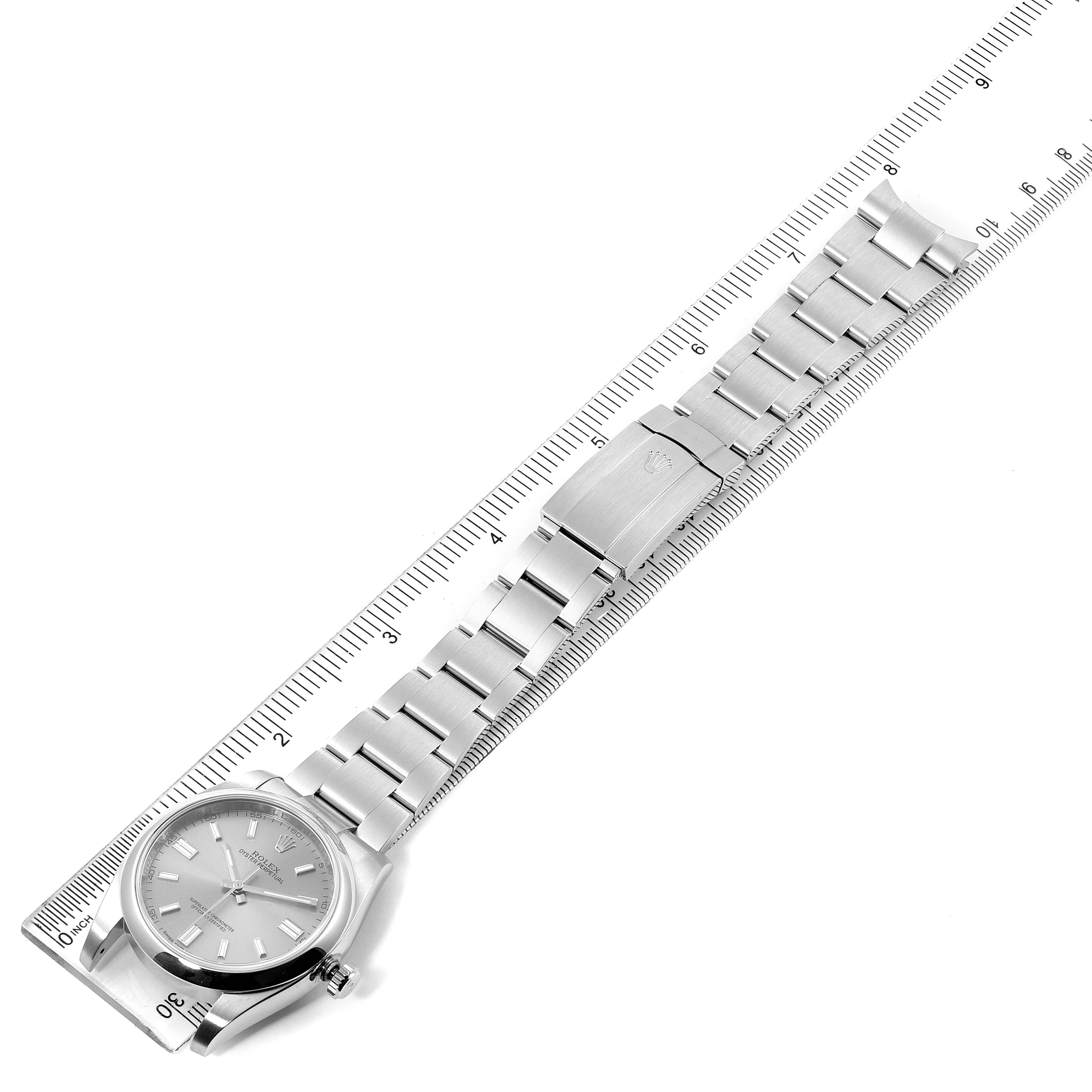 The Oyster Perpetual Rolex watch is shown in a top-down angle with its full bracelet and clasp marked against a ruler for scale.