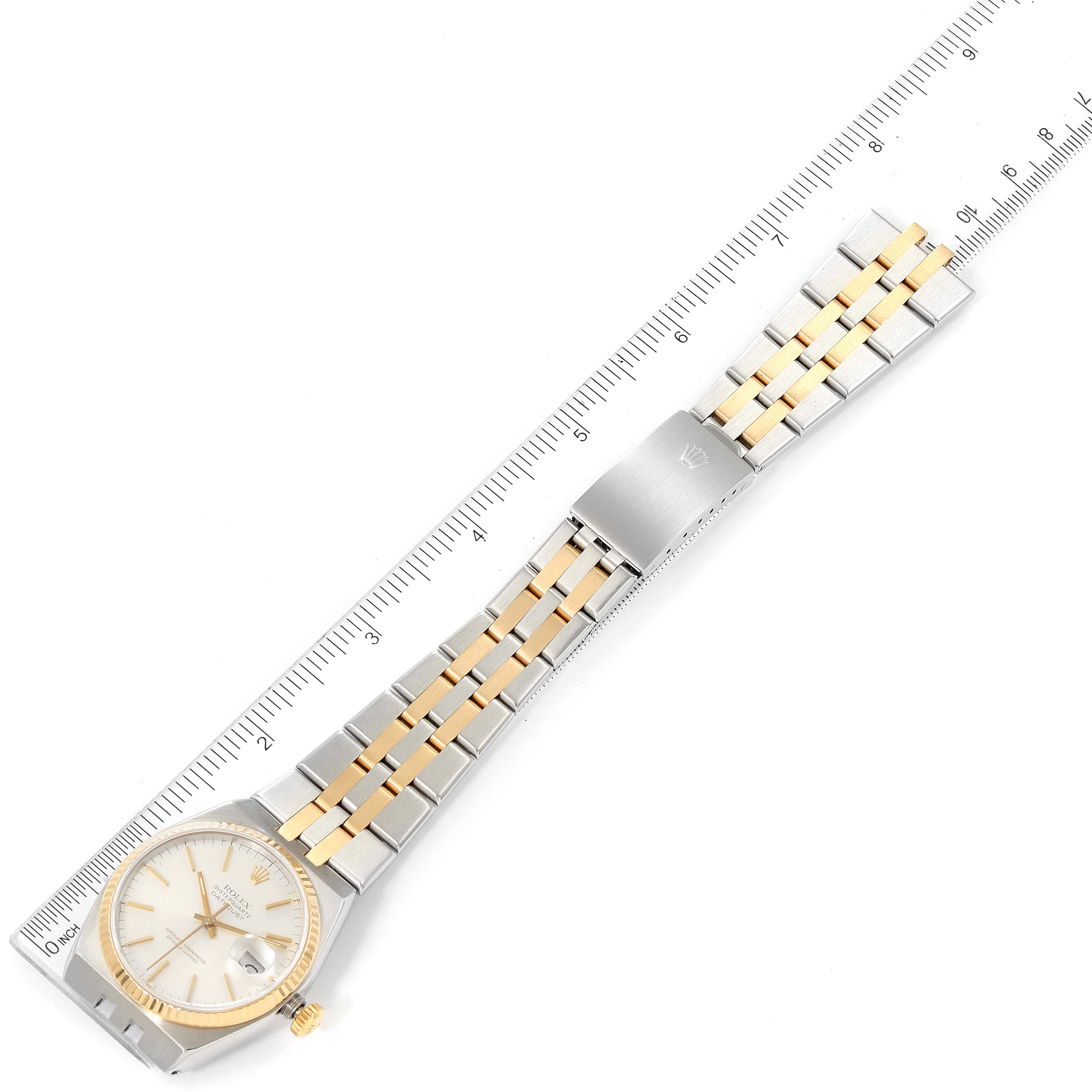 The Rolex Oysterquartz 17013 Men's Steel and Gold (two tone) Silver Dial 17013 Men's Steel and Gold (two tone) Silver Dial watch is shown laid flat with its two-tone bracelet and clasp, alongside a measurement ruler.
