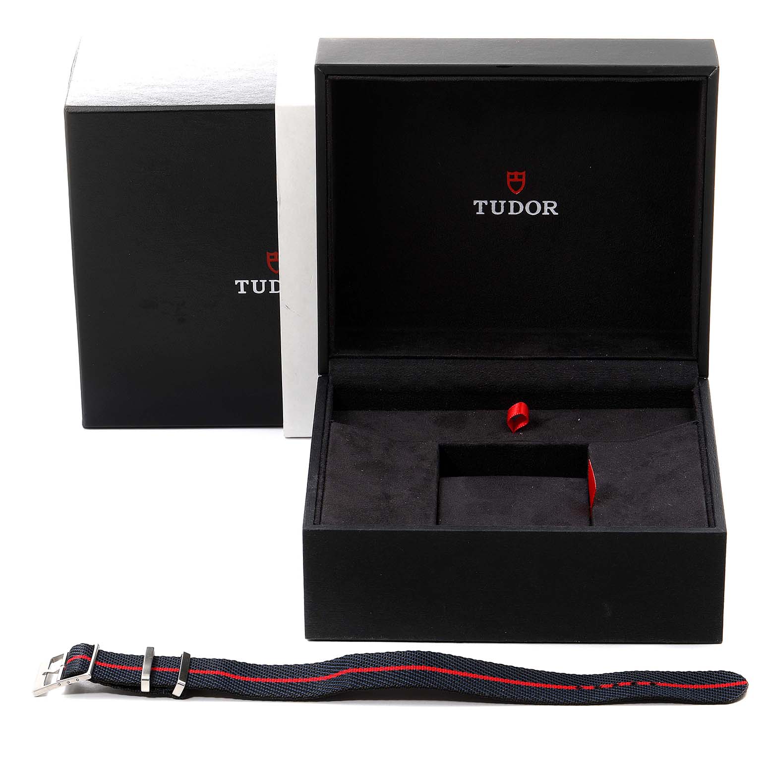 The image shows the packaging box of the Tudor Heritage Black Bay 79830RB Men
s Stainless Steel Black Dial 79830RB Men
s Stainless Steel Black Dial watch with an additional strap placed in front.