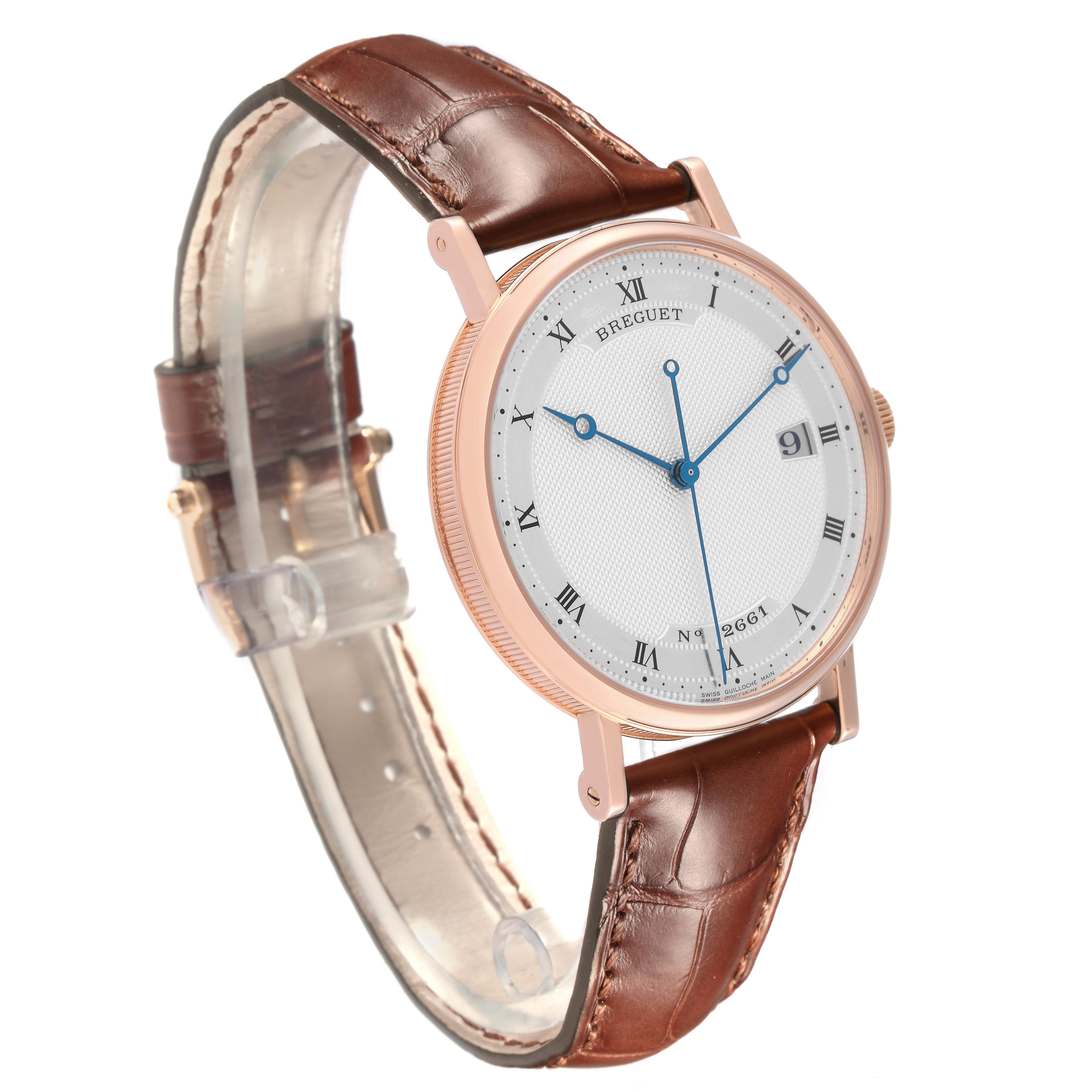 The Breguet Classique 5177BR/12/9V6 Men's Rose Gold Silver Dial 5177BR/12/9V6 Men's Rose Gold Silver Dial watch is shown at an angled view, displaying its round face, Roman numerals, blue hands, and brown leather strap.