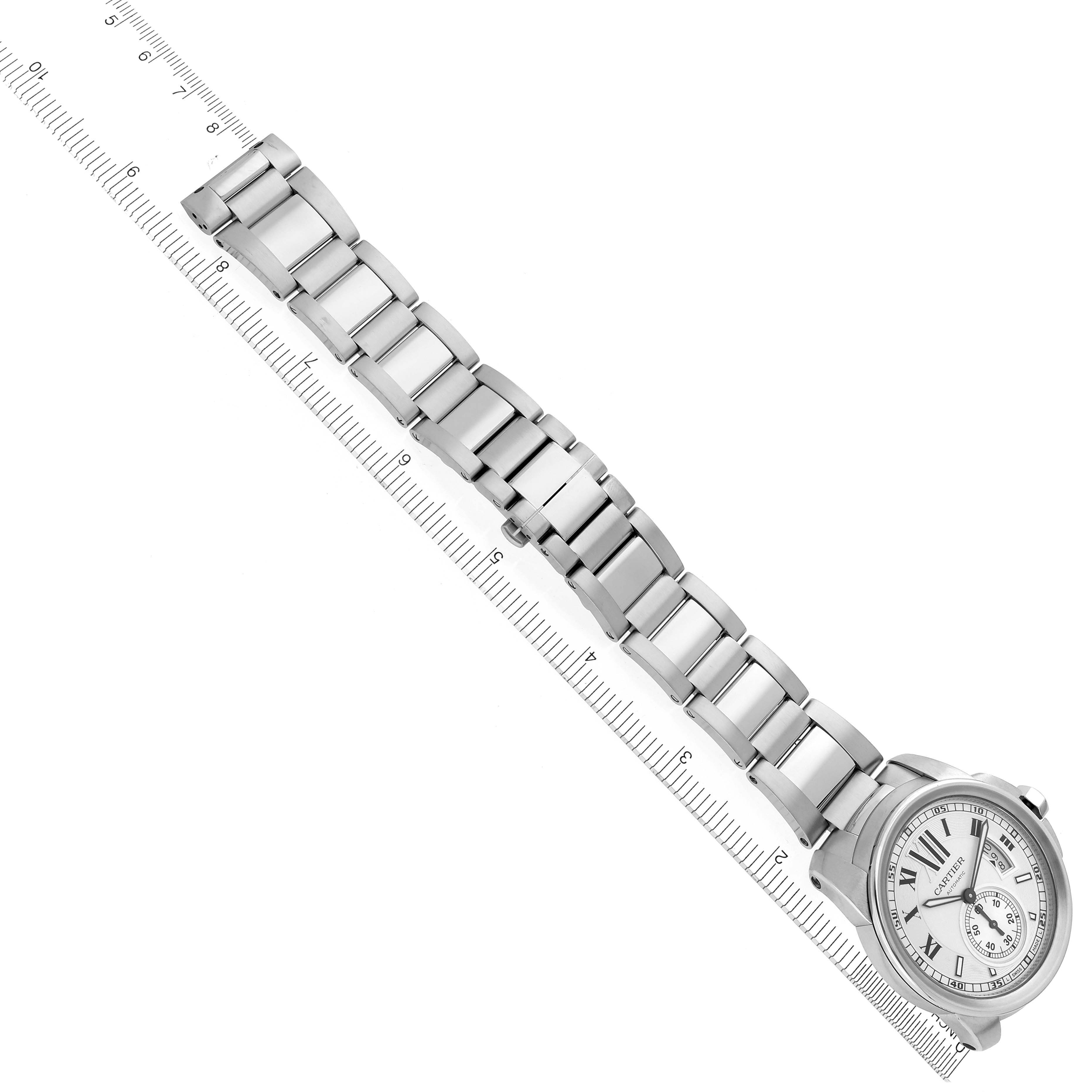 The Calibre de Cartier watch is shown from a top view, displaying the full watch face and metal bracelet aligned with a ruler.
