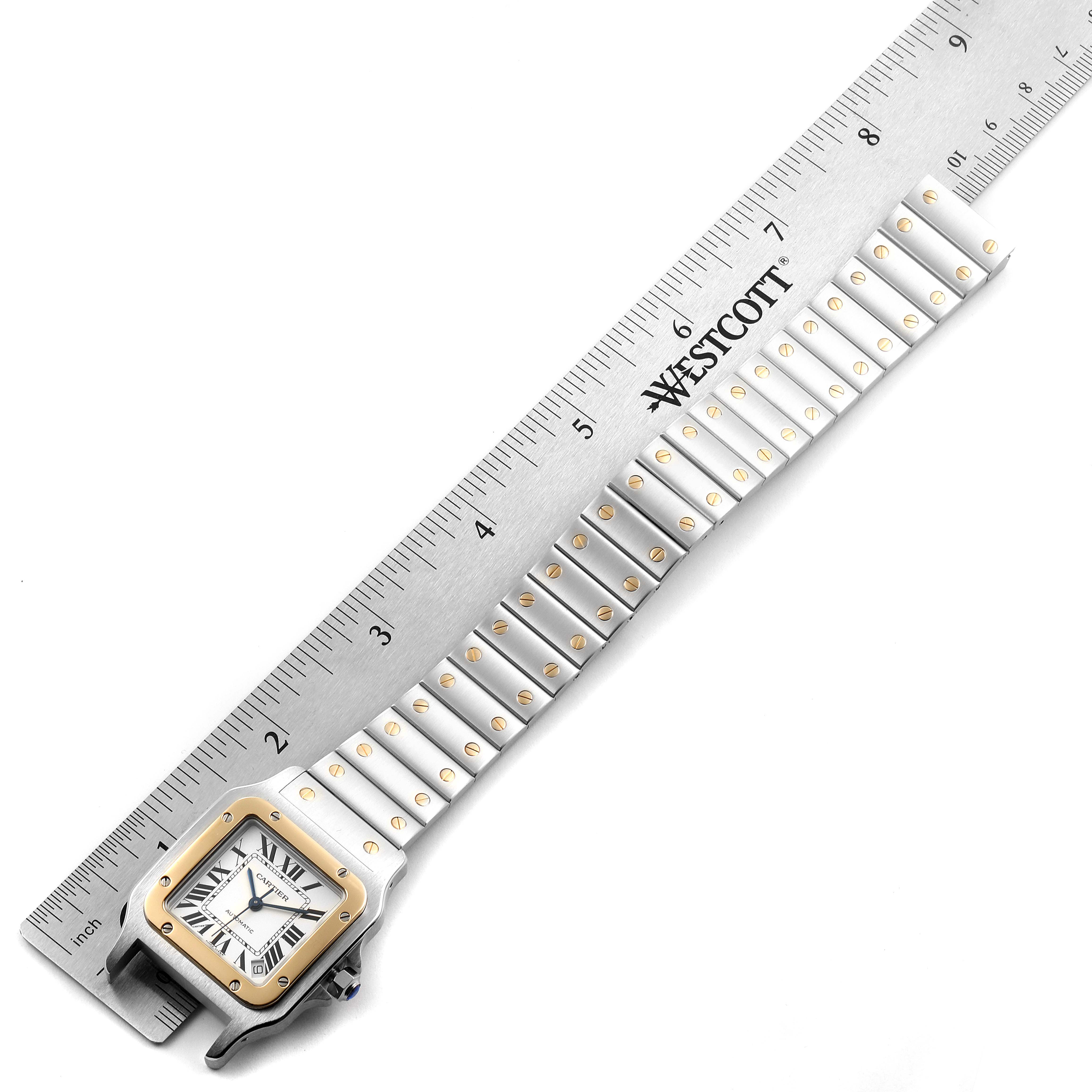 The image shows a Santos model watch by Cartier with its face and bracelet laid flat beside a ruler.