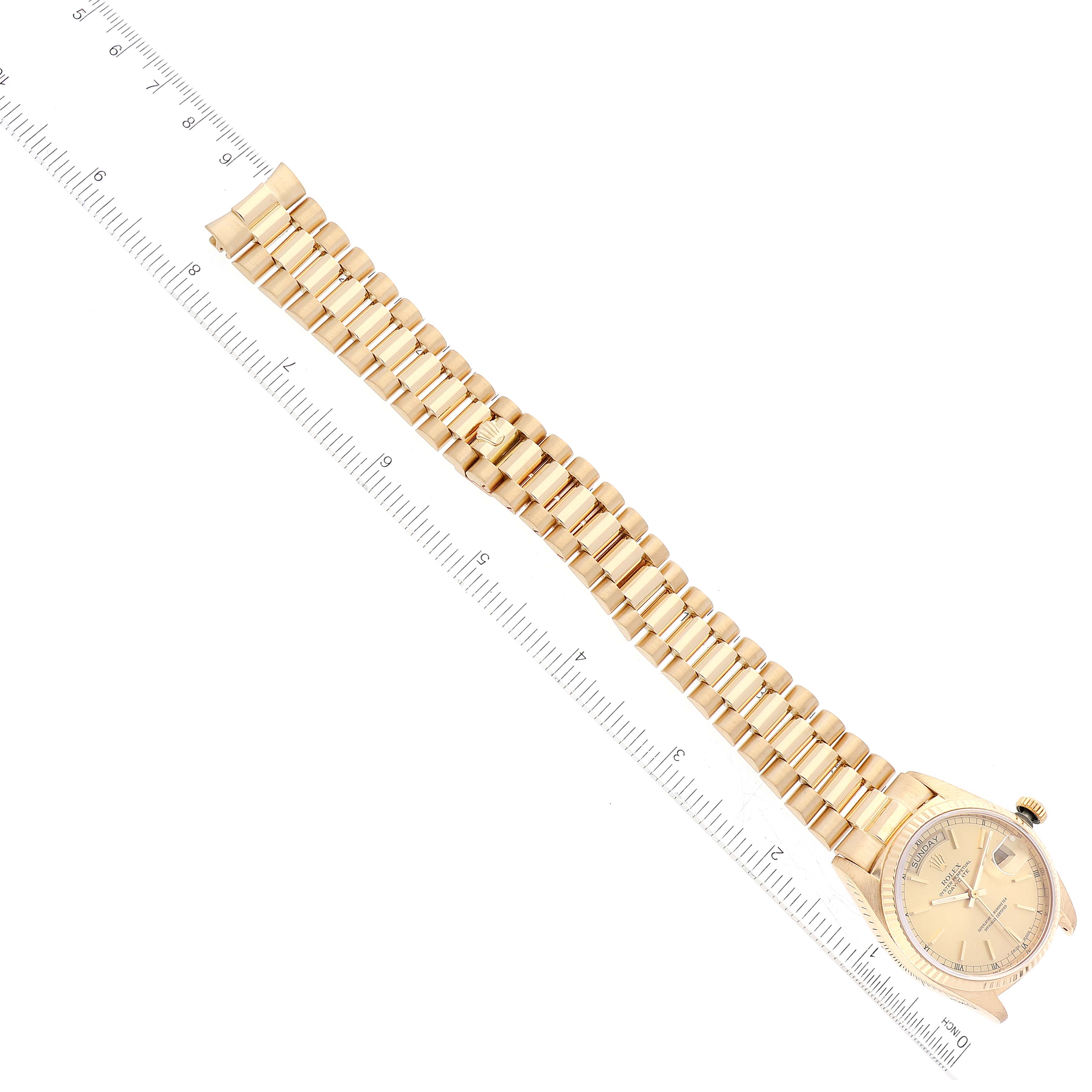 The image shows the Rolex President 18038 Men
s Yellow Gold Champagne Dial 18038 Men
s Yellow Gold Champagne Dial model watch from a top-down angle, highlighting its face and bracelet next to a ruler.