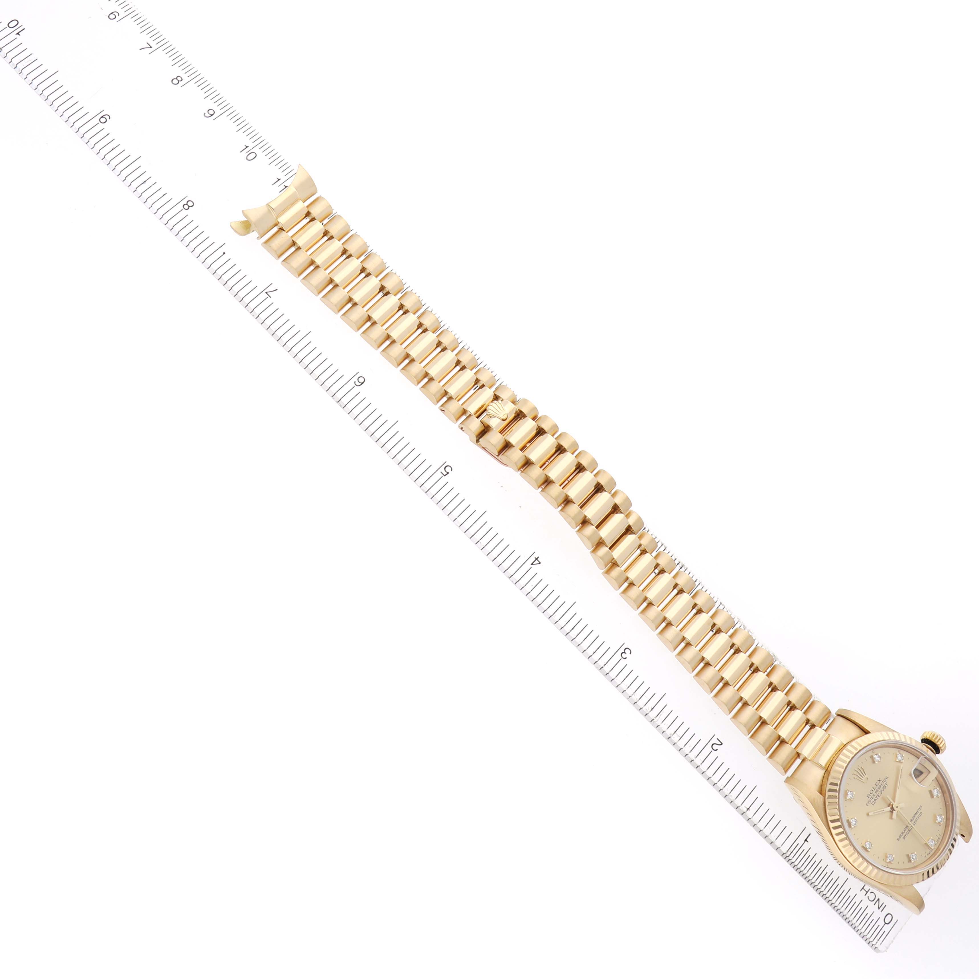 The Rolex President 68278 Women's Yellow Gold Champagne Dial watch is shown from an overhead angle, displaying the face and full gold bracelet alongside a ruler for scale.