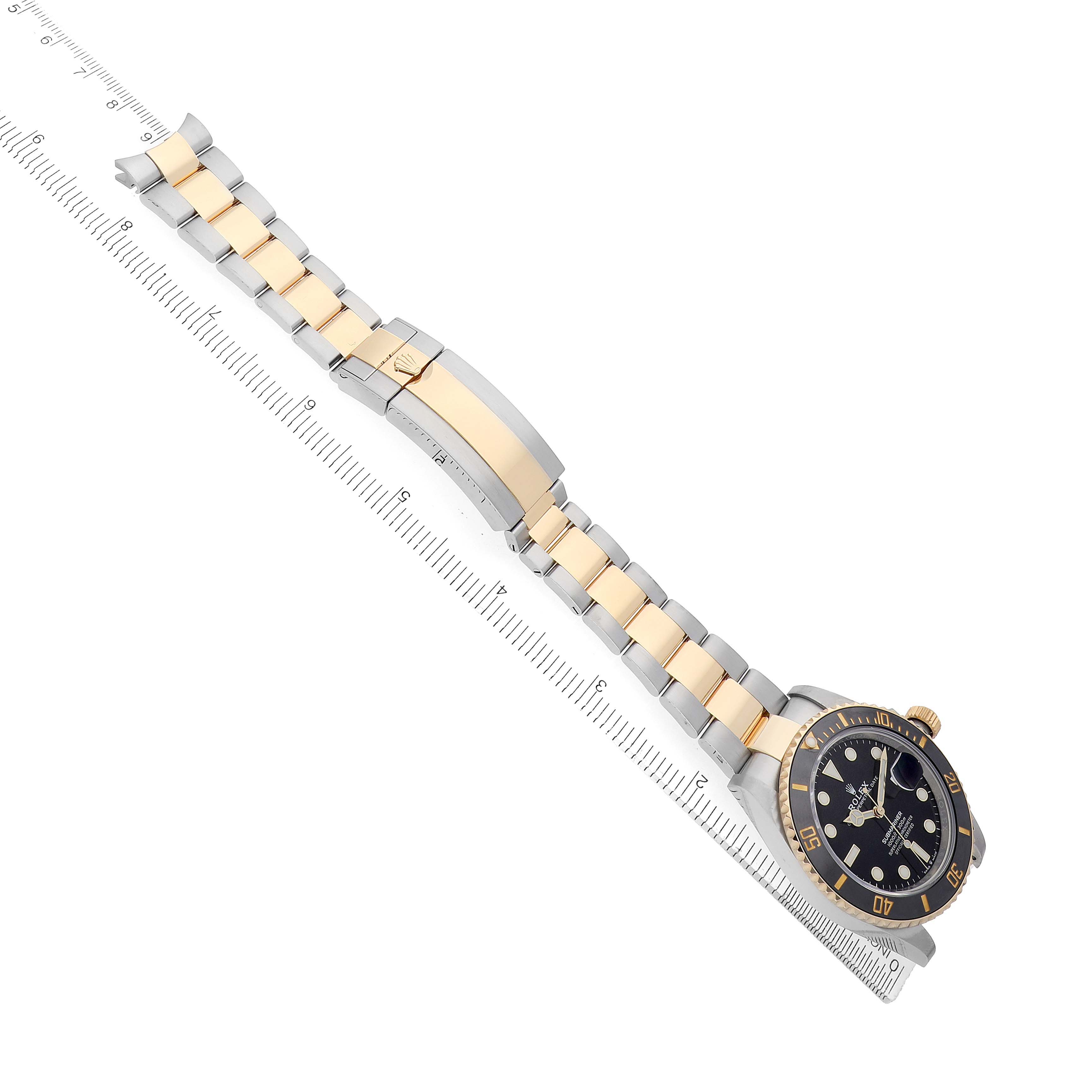 The image shows a Rolex Submariner 126613 Men's Steel and Gold (two tone) Black Dial at a diagonal angle, displaying the bracelet, clasp, and watch face against a ruler.
