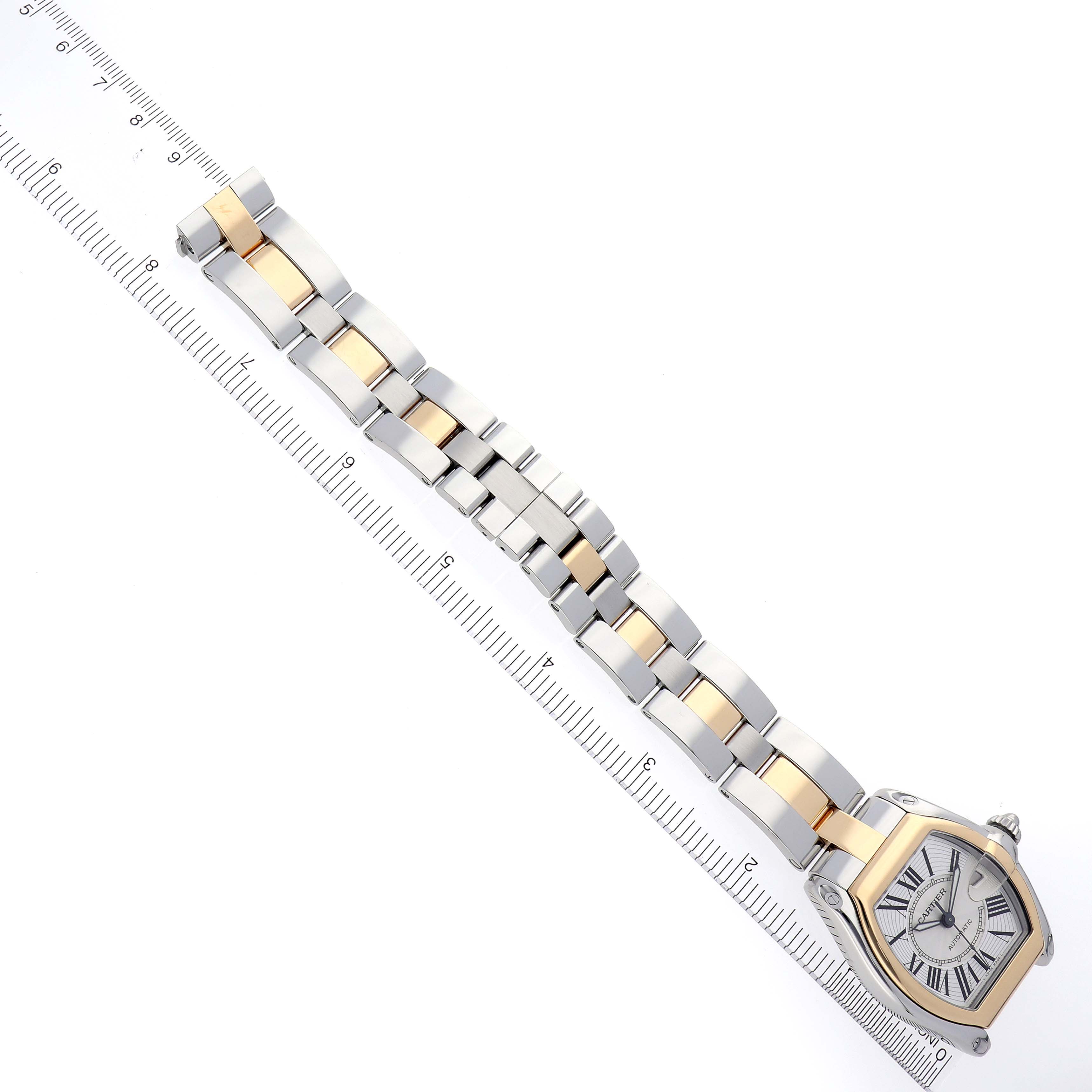 The image shows the Cartier Roadster W62031Y4 Men's Steel and Gold (two tone) Silver Dial W62031Y4 Men's Steel and Gold (two tone) Silver Dial watch from a top view, highlighting its two-tone bracelet and face beside a ruler.