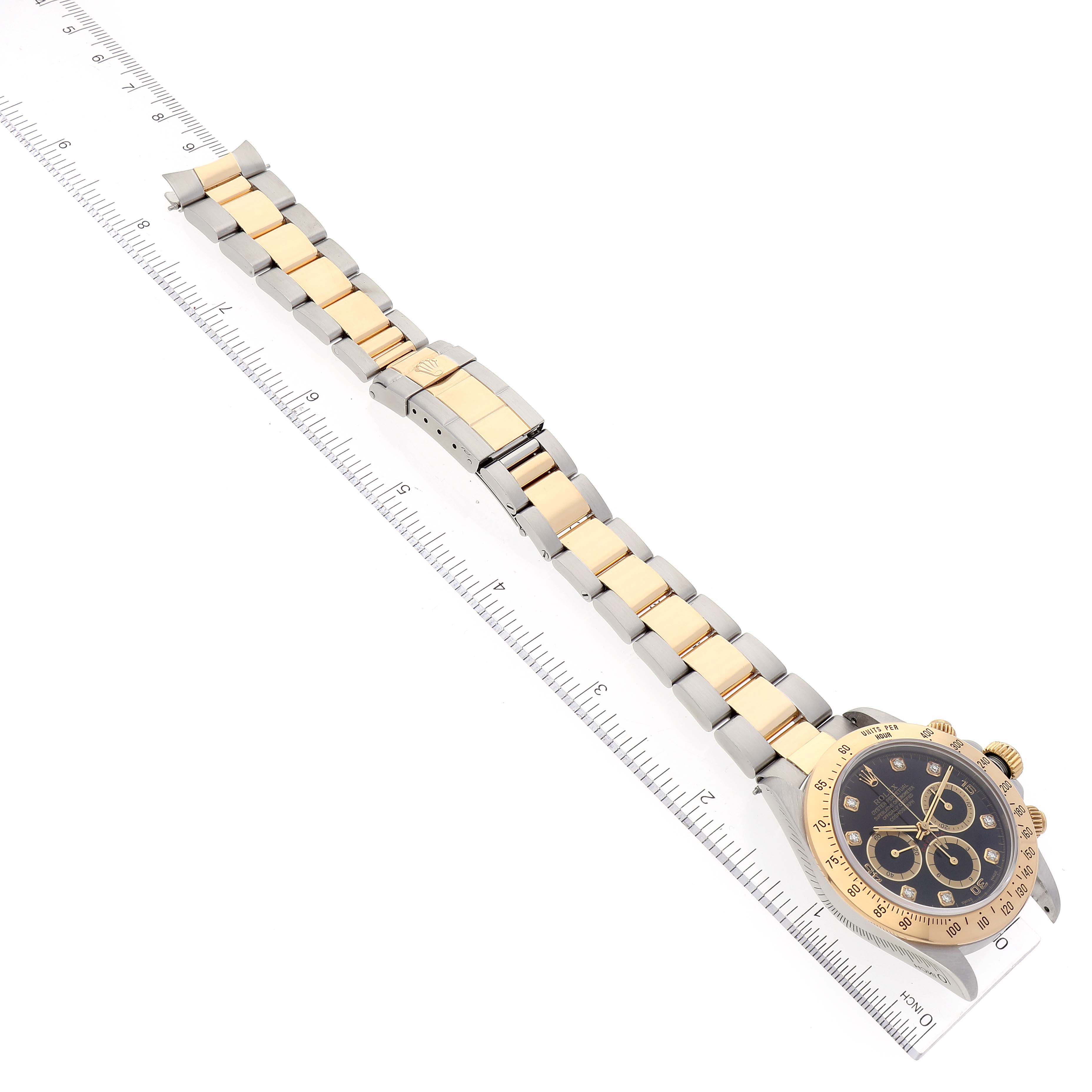 The image shows a Rolex Daytona 16523 Men's Steel and Gold (two tone) Black Dial 16523 Men's Steel and Gold (two tone) Black Dial watch laid out flat alongside a ruler, displaying the entire bracelet and dial from a top-down angle.
