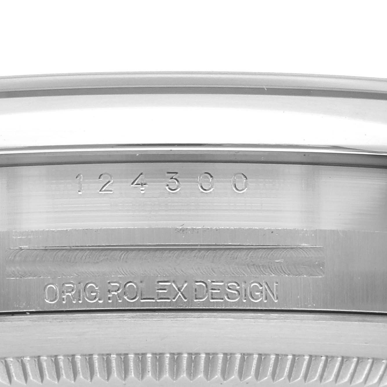 The image shows the side of the Rolex Oyster Perpetual 124300 Men's Stainless Steel Blue Dial 124300 Men's Stainless Steel Blue Dial case with engraved model number and "ORIG. ROLEX DESIGN."