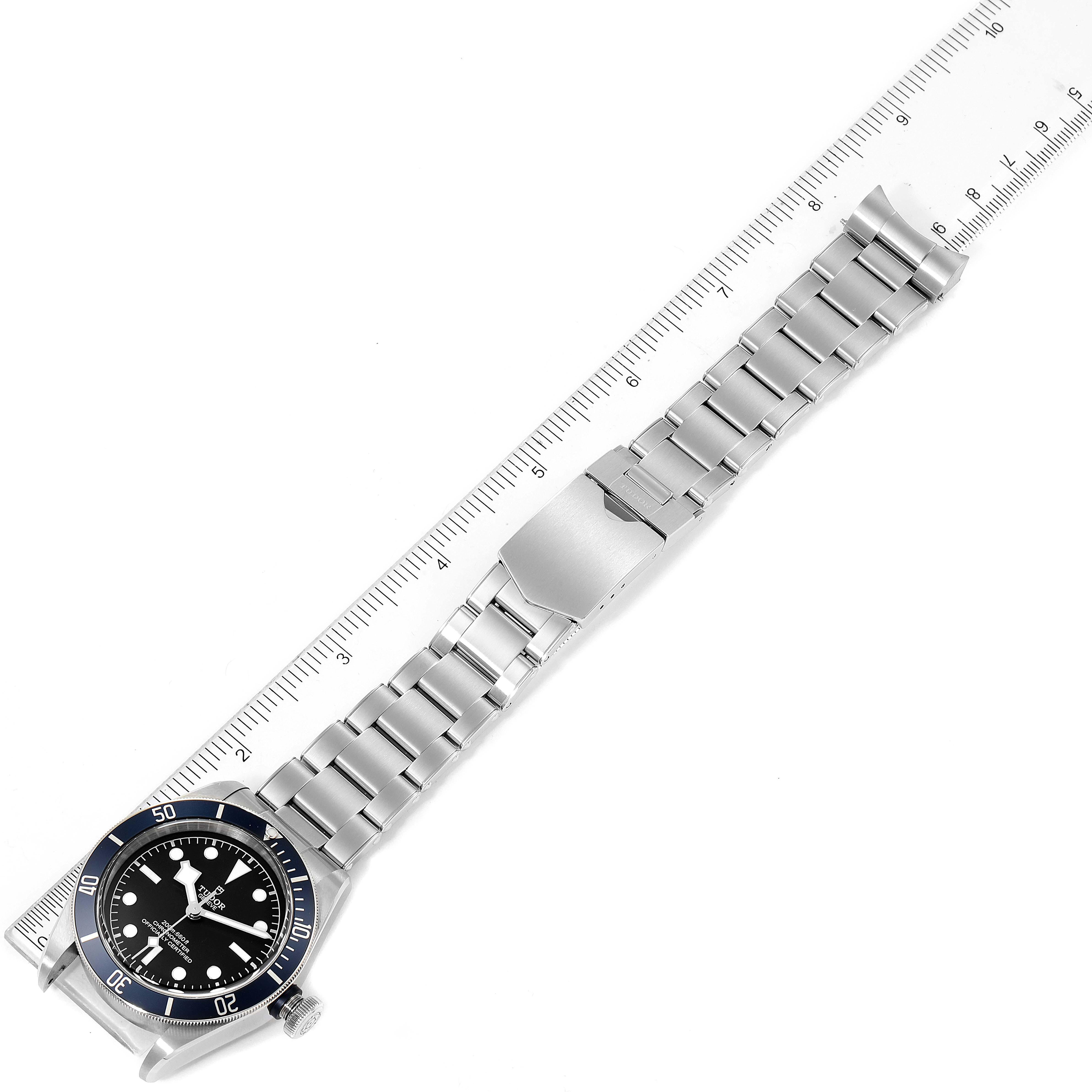 The image shows a Tudor Heritage Black Bay 79230B Men
s Stainless Steel Black Dial 79230B Men
s Stainless Steel Black Dial watch laid flat with its stainless steel band fully extended next to a ruler.