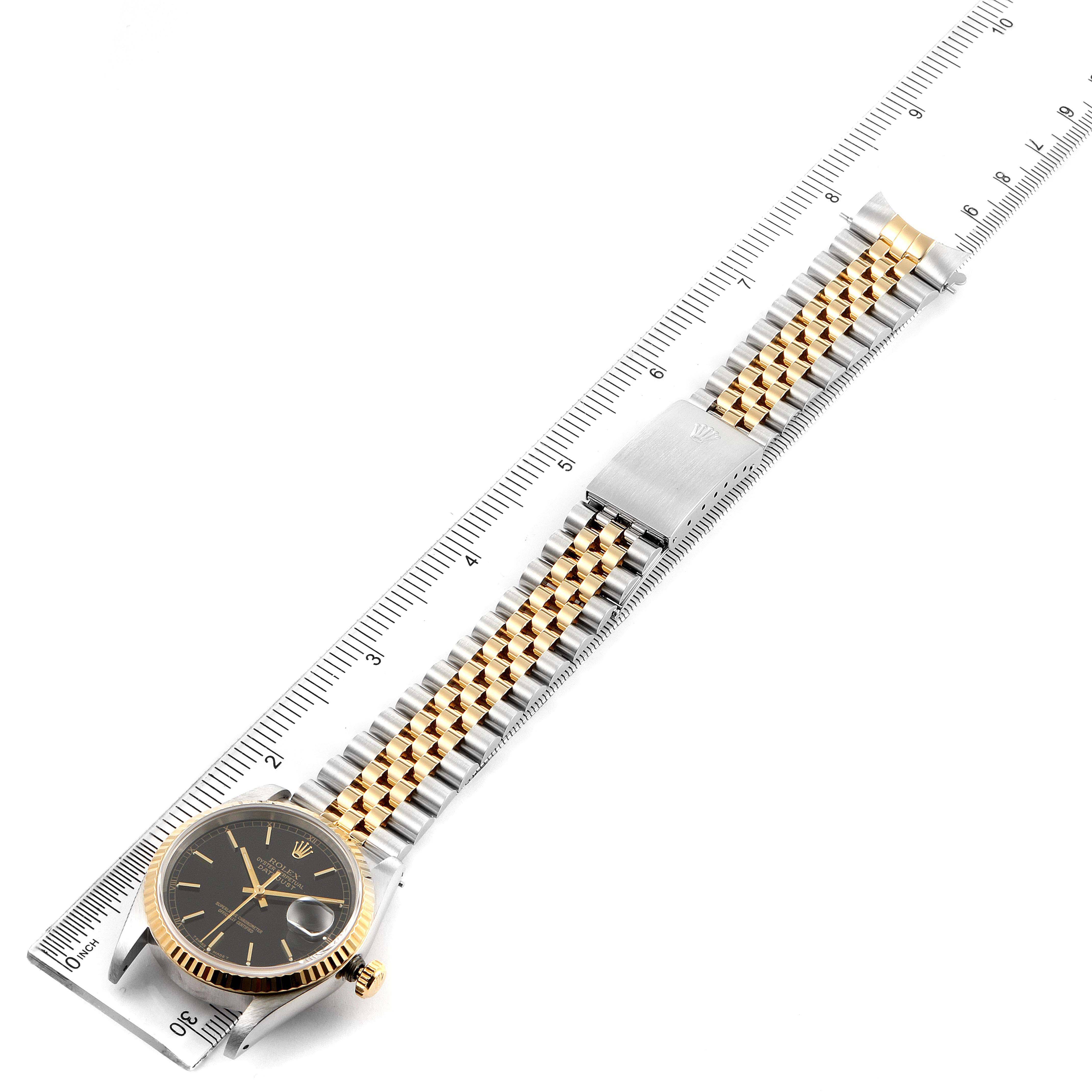 The Rolex Datejust 16233 Men's Steel and Gold (two tone) Black Dial 16233 Men's Steel and Gold (two tone) Black Dial watch is shown from a top-down angle with its bezel, dial, and entire bracelet visible, alongside a ruler.