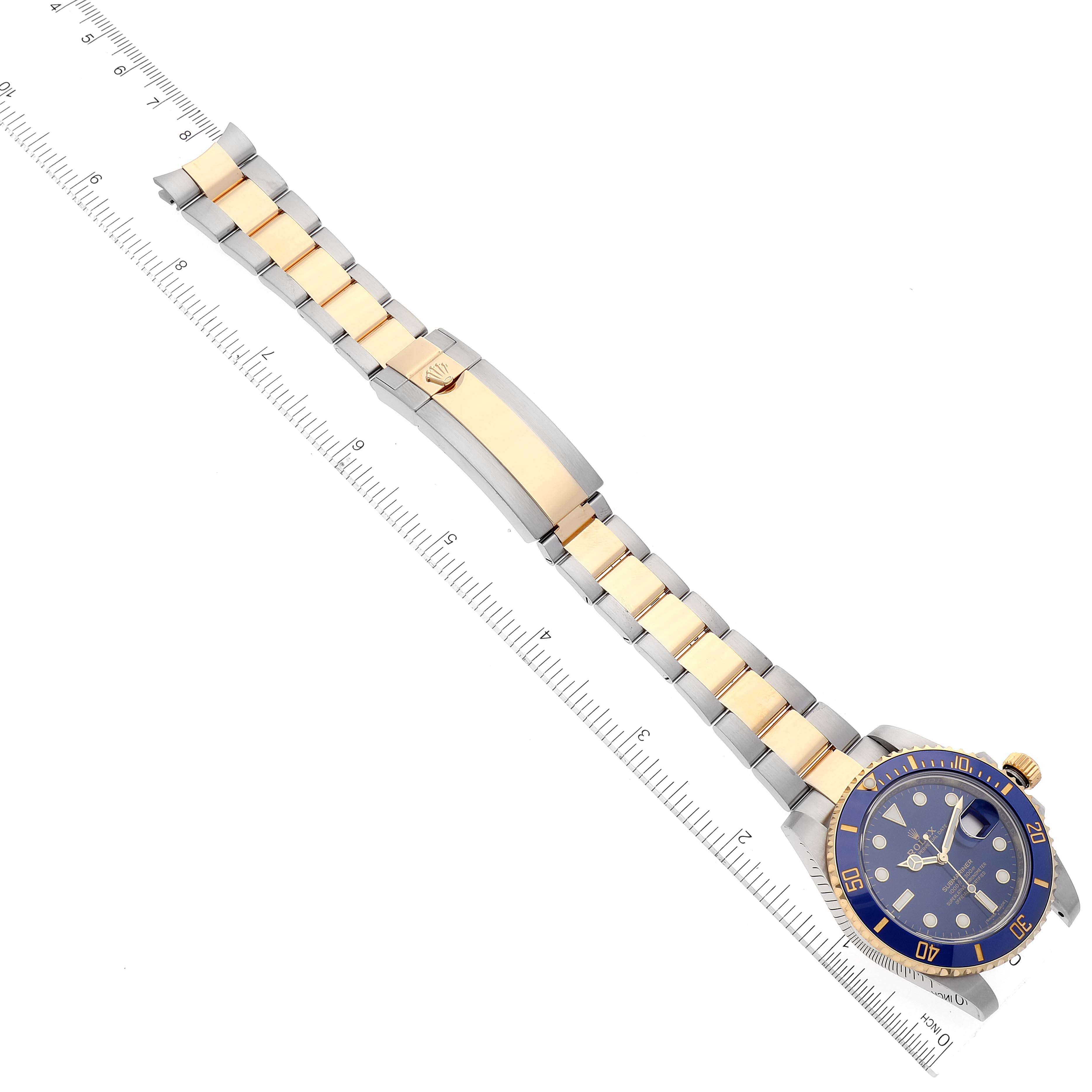 The image shows a Rolex Submariner 116613 Men's Steel and Gold (two tone) Blue Dial 116613 Men's Steel and Gold (two tone) Blue Dial watch with a two-tone bracelet, clasp, and blue dial, positioned next to a ruler.