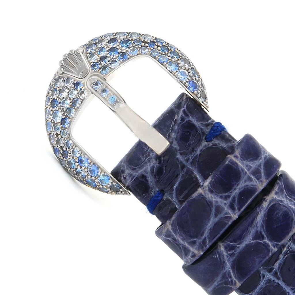 The image shows a close-up of the Rolex Cellini 6201 Women's White Gold Mother of Pearl Dial 6201 Women's White Gold Mother of Pearl Dial watch buckle with blue gemstone decorations and a textured blue strap.