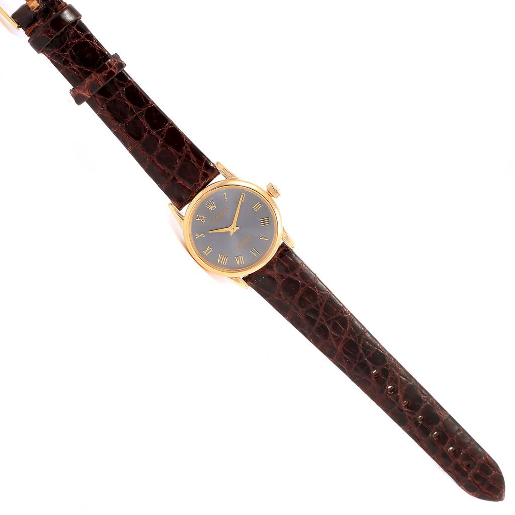 The image shows a Rolex Cellini 6111 Women's Yellow Gold Grey Dial 6111 Women's Yellow Gold Grey Dial watch at a slightly angled top-down view, featuring its gold case, black dial, and brown leather strap.