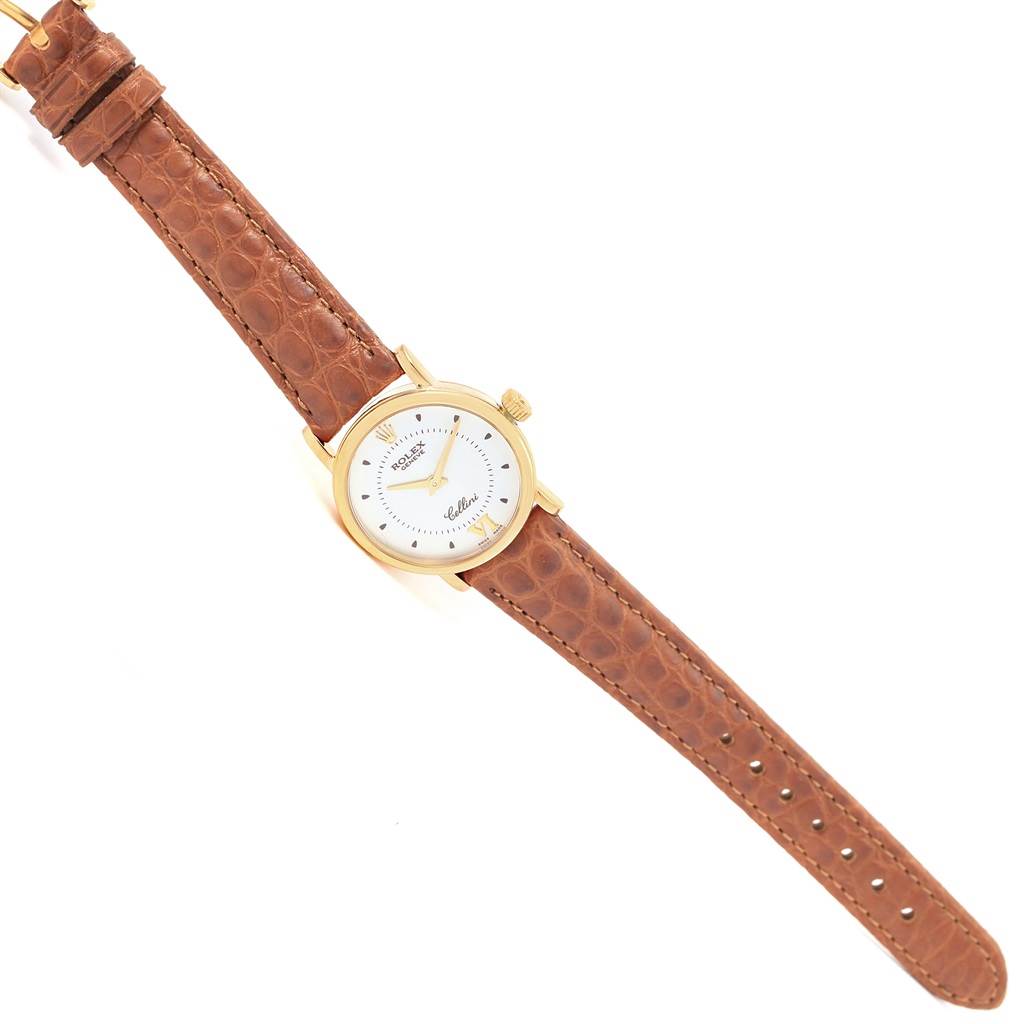 The image shows a Rolex Cellini 6610 Women's Yellow Gold Silver Dial 6610 Women's Yellow Gold Silver Dial watch from a top-down angle, featuring its brown leather strap, gold case, and white dial.