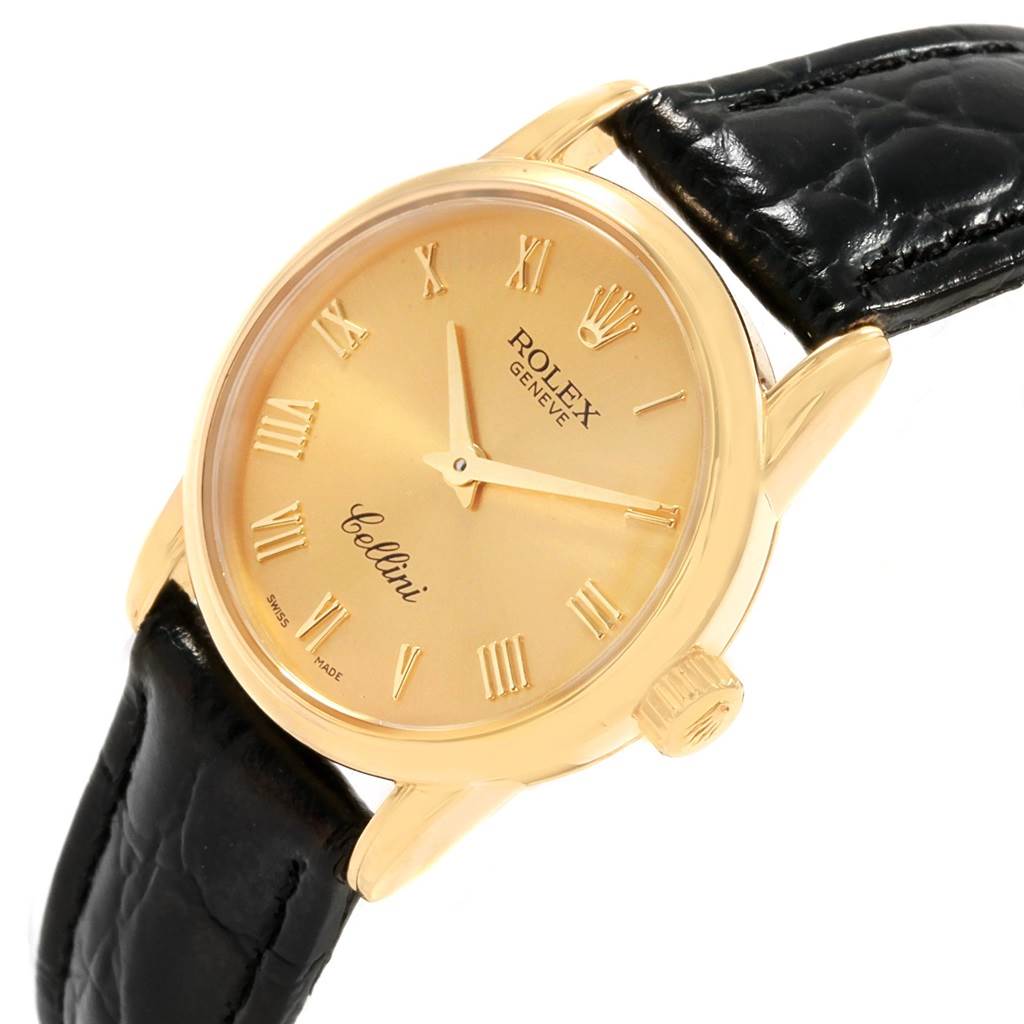 The image shows a close-up of a Rolex Cellini 6111 Women's Yellow Gold Champagne Dial 6111 Women's Yellow Gold Champagne Dial watch with a gold dial and a black leather strap, displaying the crown and hands.