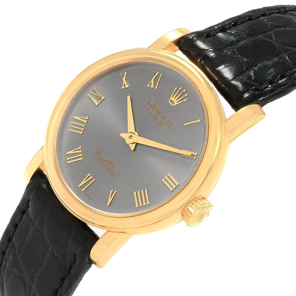 The image shows a Rolex Cellini 6110 Women
s Yellow Gold Grey Dial 6110 Women
s Yellow Gold Grey Dial watch at an angled view, highlighting its gold case, black strap, and grey dial with Roman numerals.