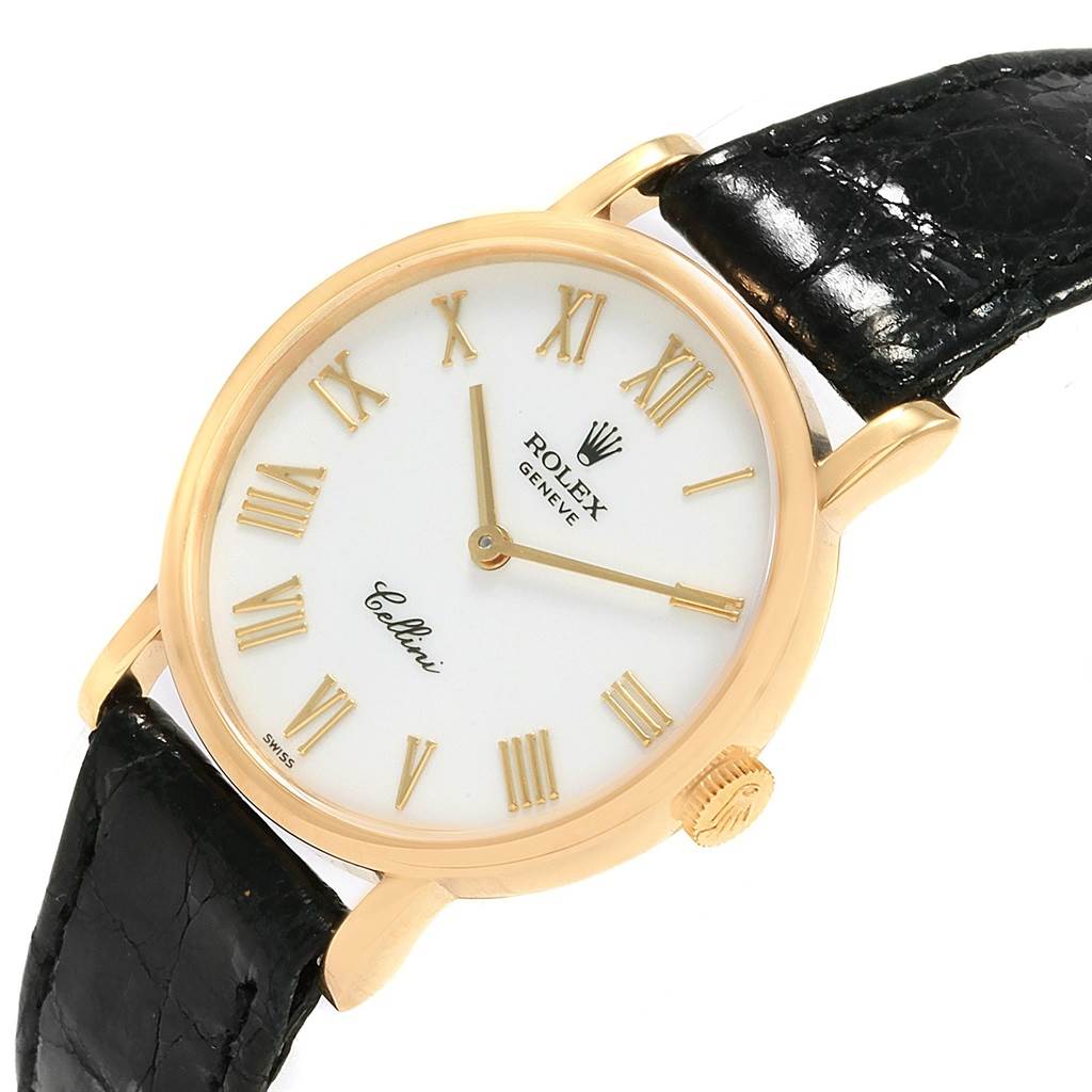 The Cellini model by Rolex is shown at an angled view, highlighting its white dial, gold case, Roman numerals, and black leather strap.