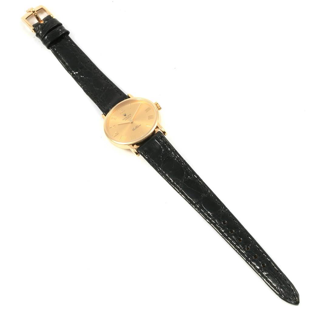 The Rolex Cellini 5109 Women's Yellow Gold Champagne Dial 5109 Women's Yellow Gold Champagne Dial watch is shown from a top-down angle, displaying the face, black leather strap, and gold buckle.