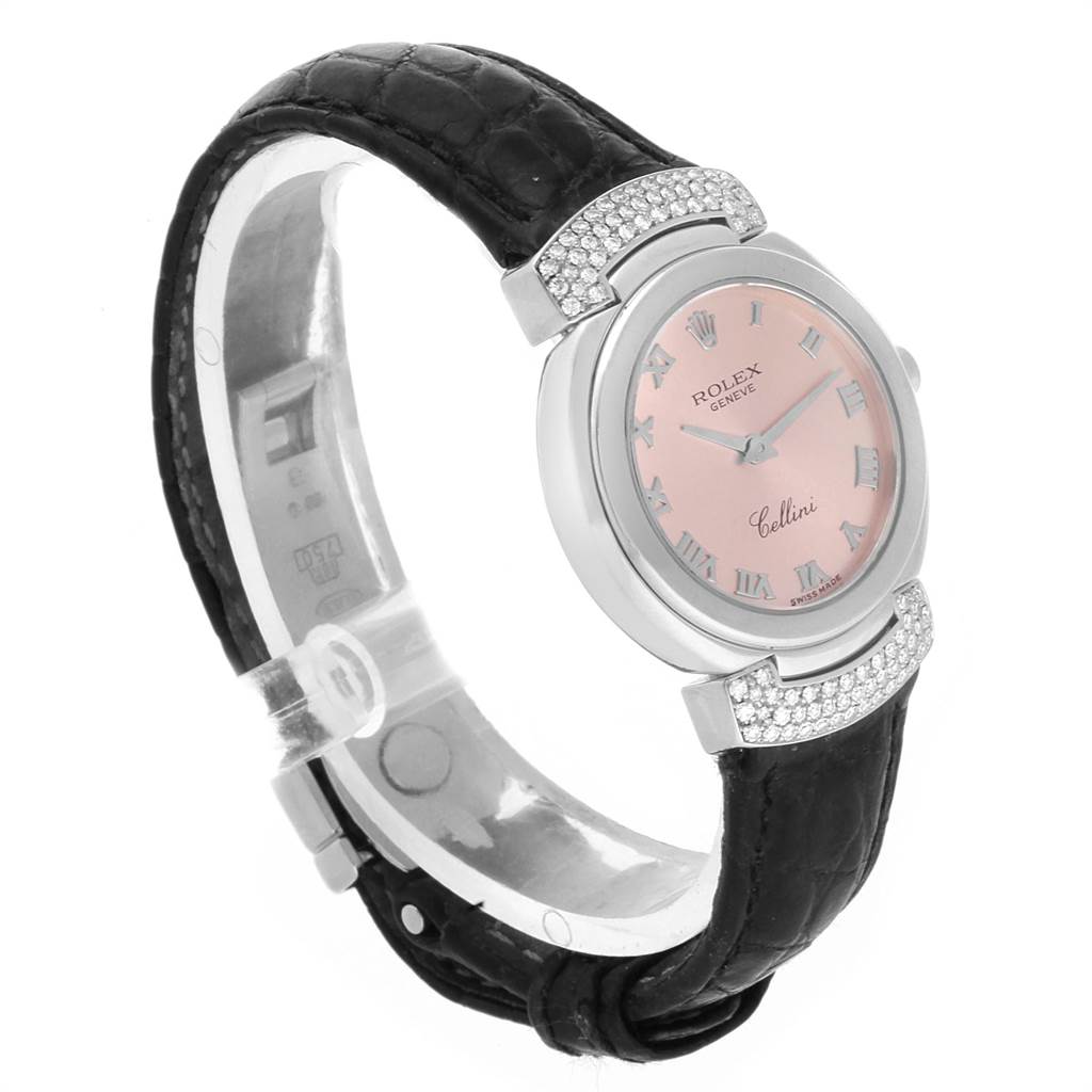 This Rolex Cellini 6672 Women's White Gold Pink Dial 6672 Women's White Gold Pink Dial watch is displayed from a side angle, showing its pink dial, Roman numerals, diamond-studded bezel, and black leather strap.