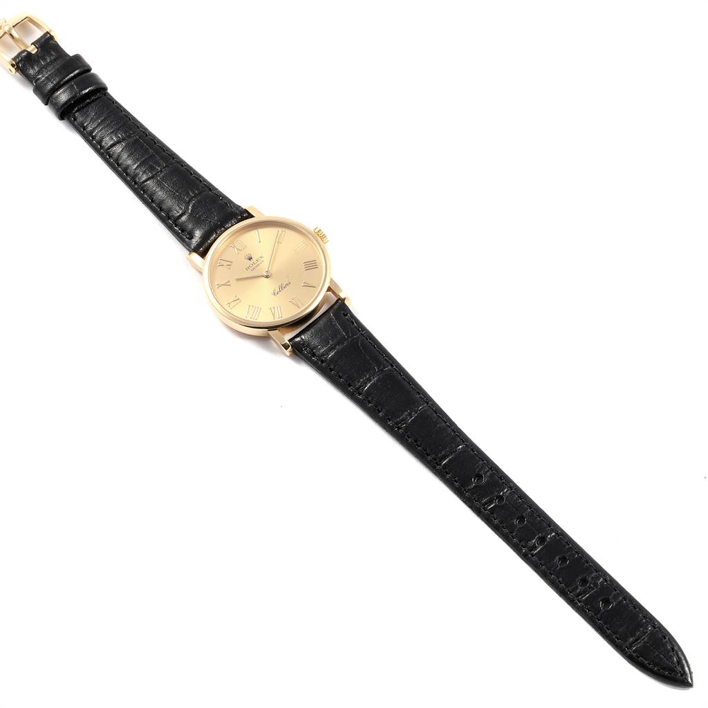 The Rolex Cellini 5109 Women's Yellow Gold Champagne Dial 5109 Women's Yellow Gold Champagne Dial watch is shown from a top-down angle, featuring a gold dial and black leather strap.