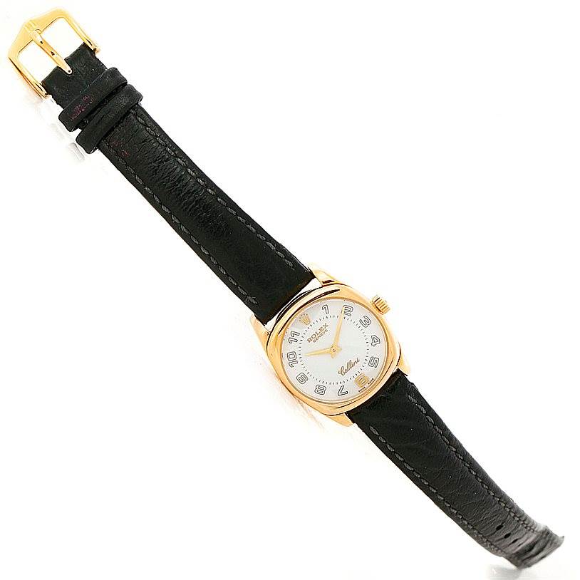 The Cellini model by Rolex is shown at an angle displaying the full watch, including the dial, black leather strap, and gold buckle.