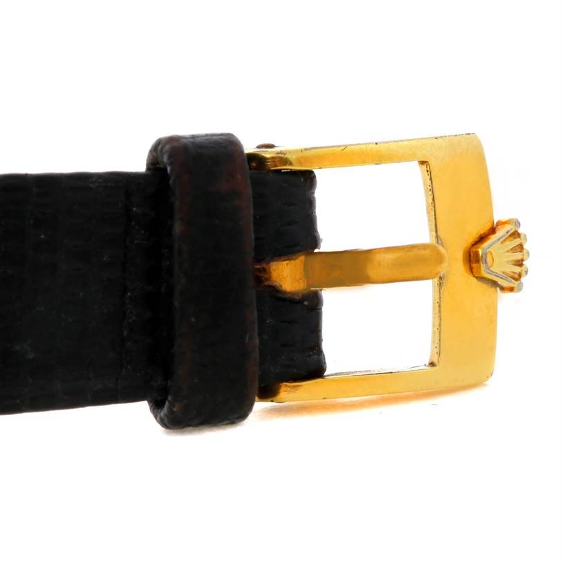 This image shows a close-up of the gold buckle and black leather strap from a Cellini model by Rolex.