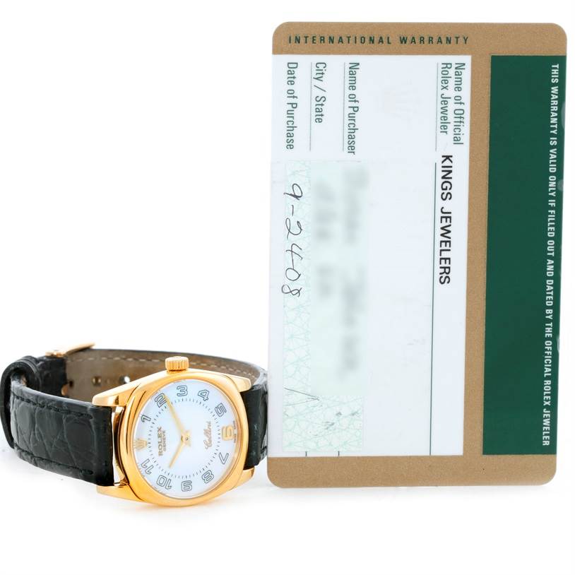 This image shows the front of a Rolex Cellini 6229 Women's Yellow Gold White Dial 6229 Women's Yellow Gold White Dial watch with its warranty card in the background.