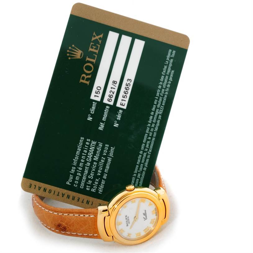 The image shows the top view of a Rolex Cellini 6621 Women's Yellow Gold White Dial 6621 Women's Yellow Gold White Dial watch with a green Rolex warranty card placed behind it.