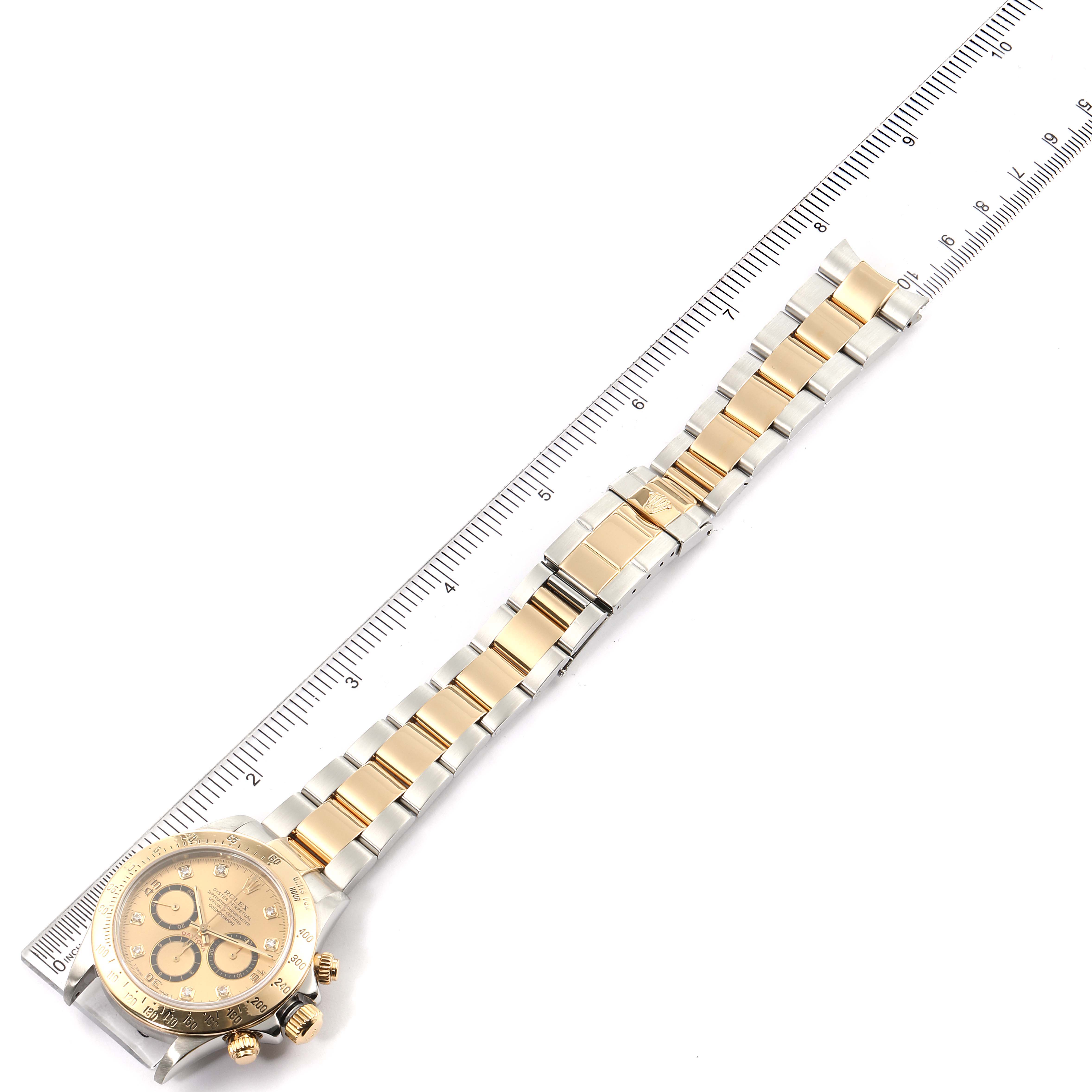The image shows a Rolex Daytona 16523 Men
s Steel and Gold (two tone) Champagne Dial 16523 Men
s Steel and Gold (two tone) Champagne Dial watch laid flat next to a ruler, displaying the watch face and full bracelet.