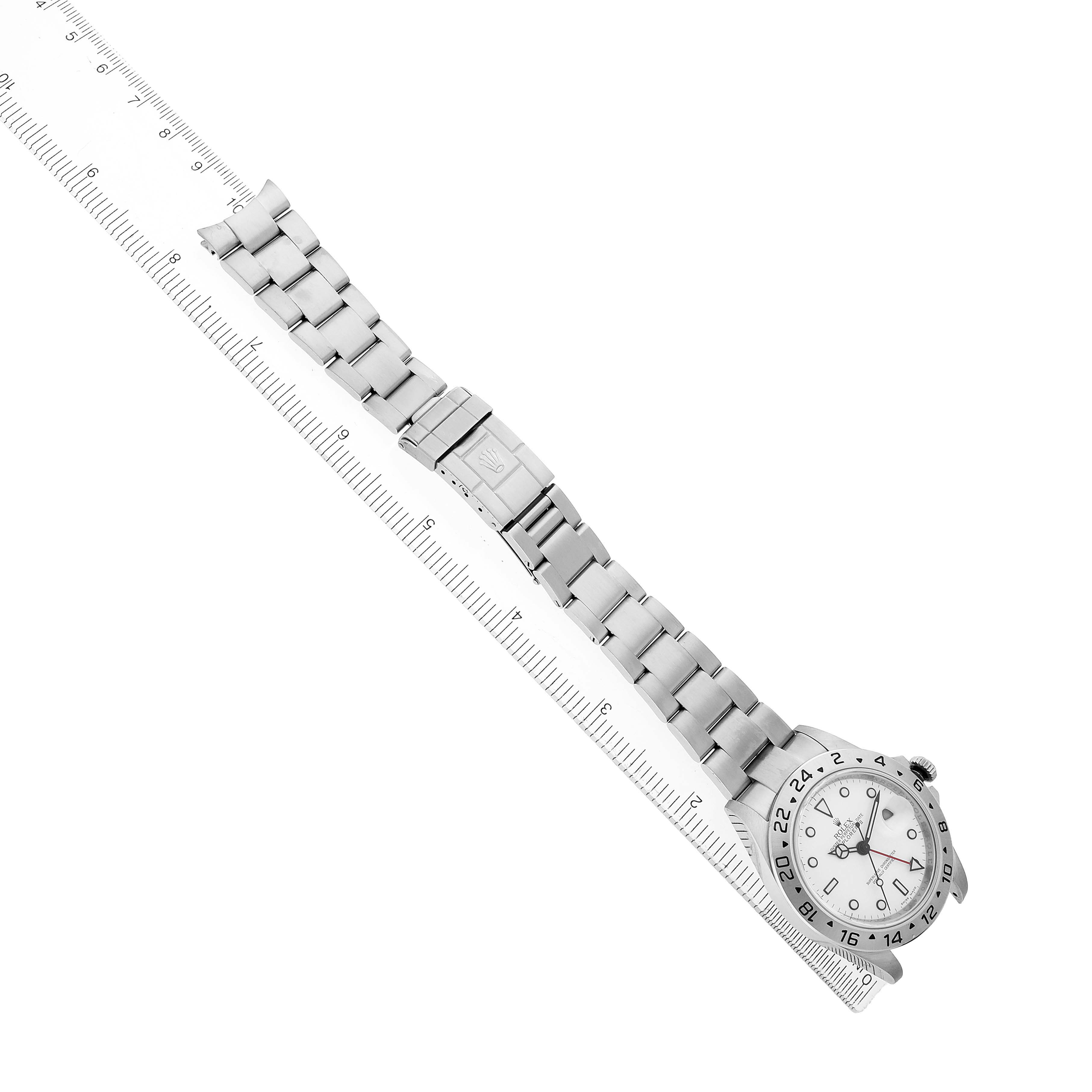 The Rolex Explorer 16570 Men's Stainless Steel White Dial watch is shown diagonally, displaying the face, bezel, and full metal bracelet alongside a ruler.