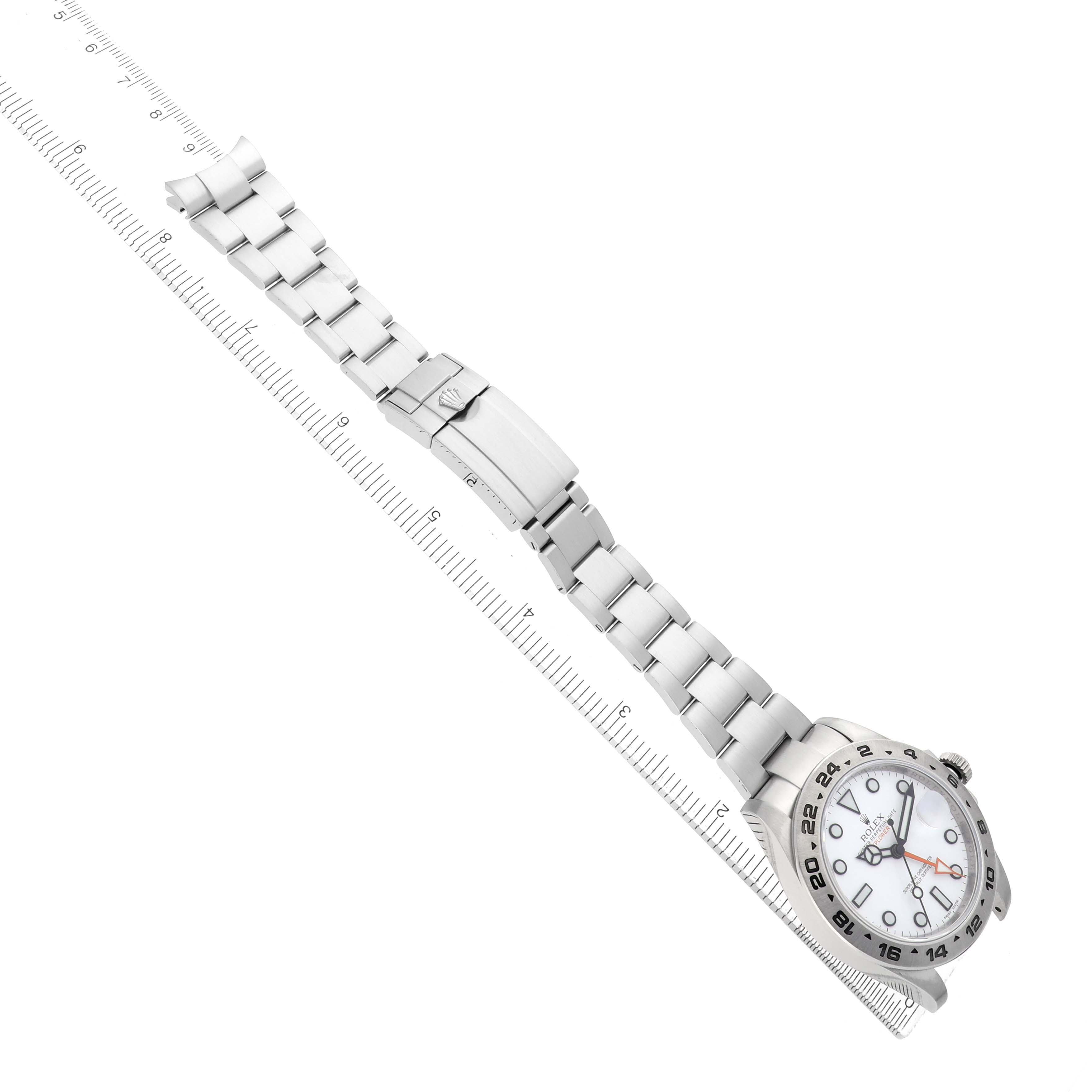 The Rolex Explorer 216570 Men's Stainless Steel White Dial watch is shown from a top-down angle, displaying its full bracelet and clasp alongside a ruler for scale.