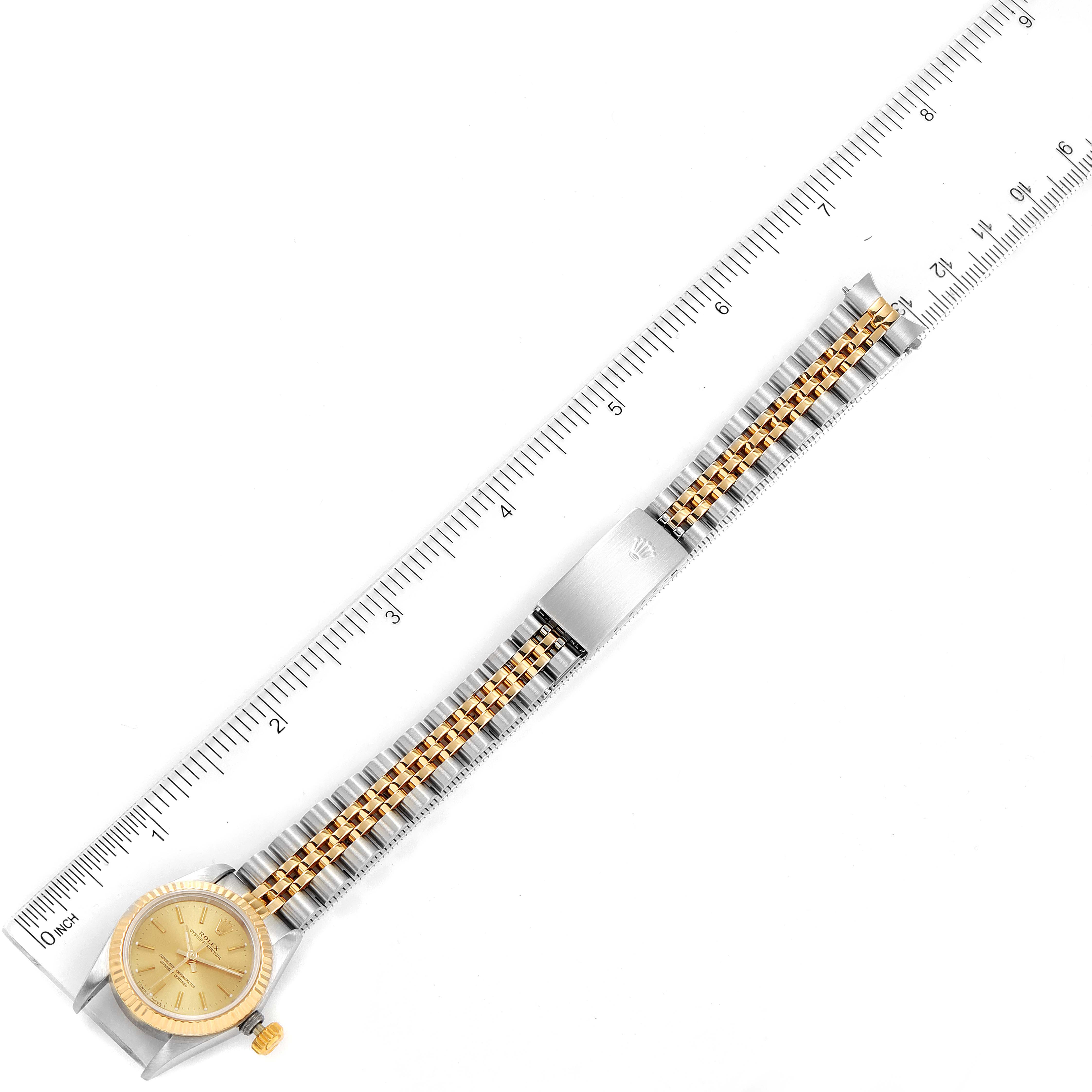 The image shows a top-down view of a Rolex Oyster Perpetual 67193 Women's Steel and Gold (two tone) Champagne Dial 67193 Women's Steel and Gold (two tone) Champagne Dial watch, revealing the face, crown, bracelet, and clasp, next to a ruler.