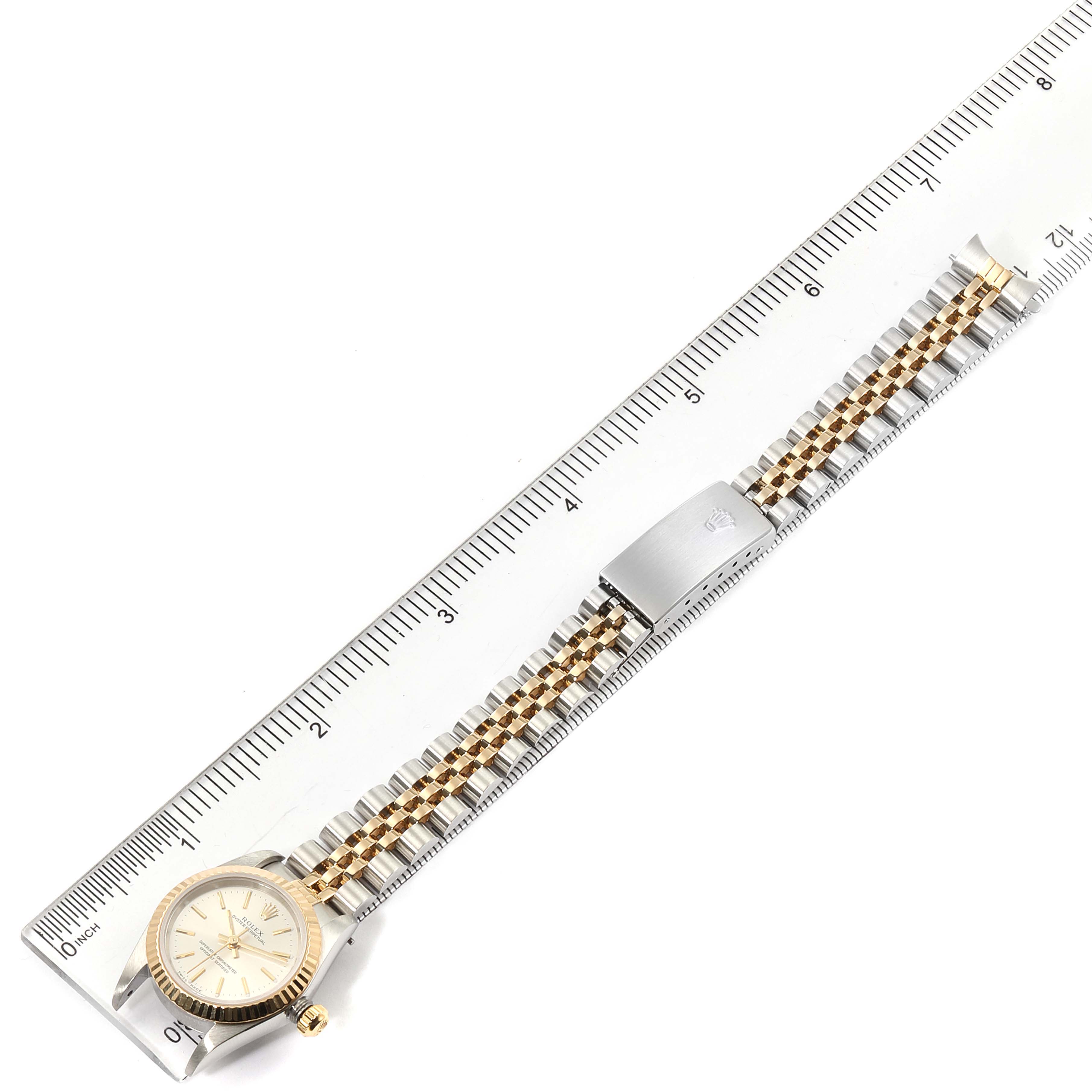 The image shows a top view of the Rolex Oyster Perpetual 76193 Women's Steel and Gold (two tone) Silver Dial 76193 Women's Steel and Gold (two tone) Silver Dial watch, including the face and the full length of the band compared with a ruler.