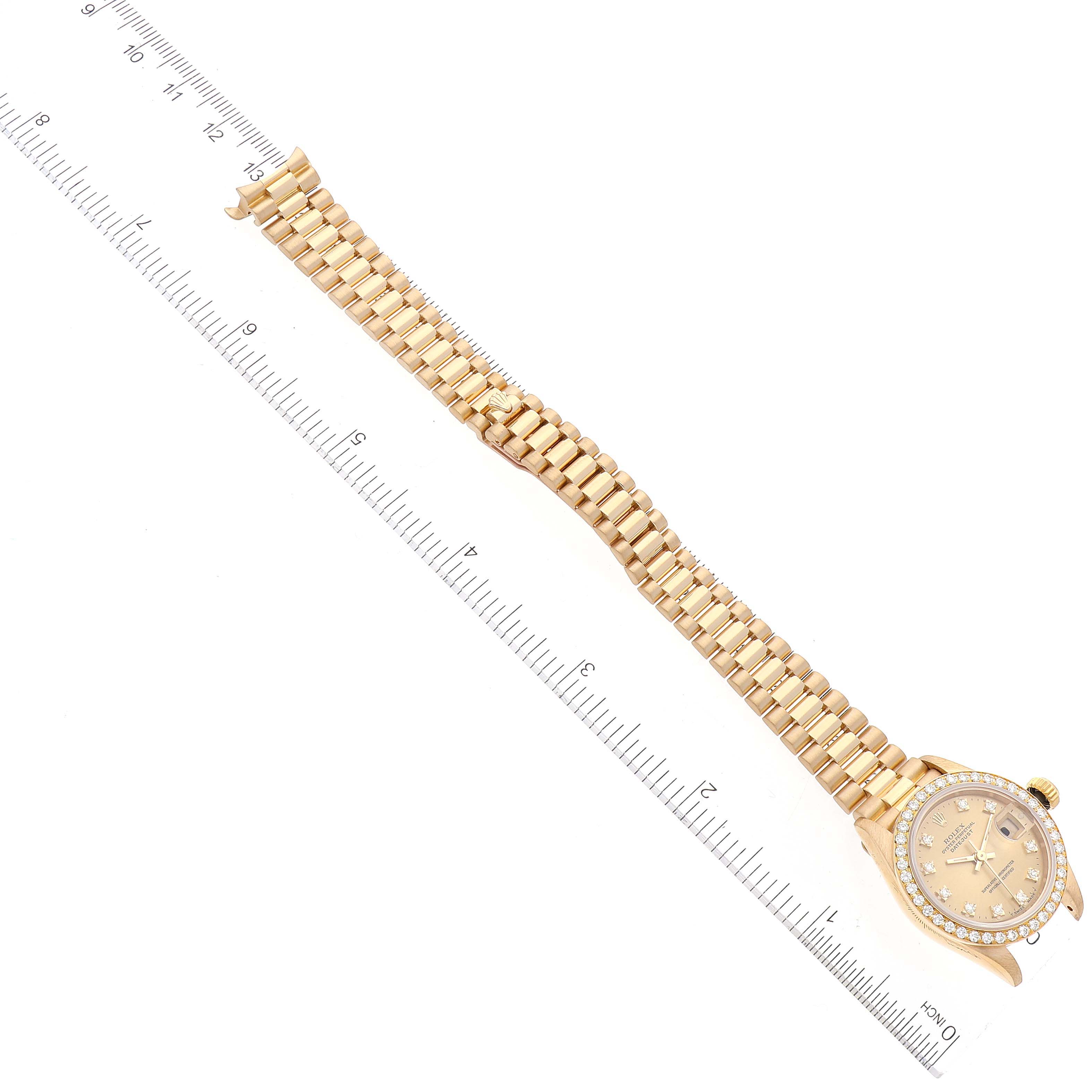 The image shows a Rolex President 69138 Women
s Yellow Gold Champagne Dial 69138 Women
s Yellow Gold Champagne Dial model watch laying flat with its full band and face visible, alongside a ruler for scale.