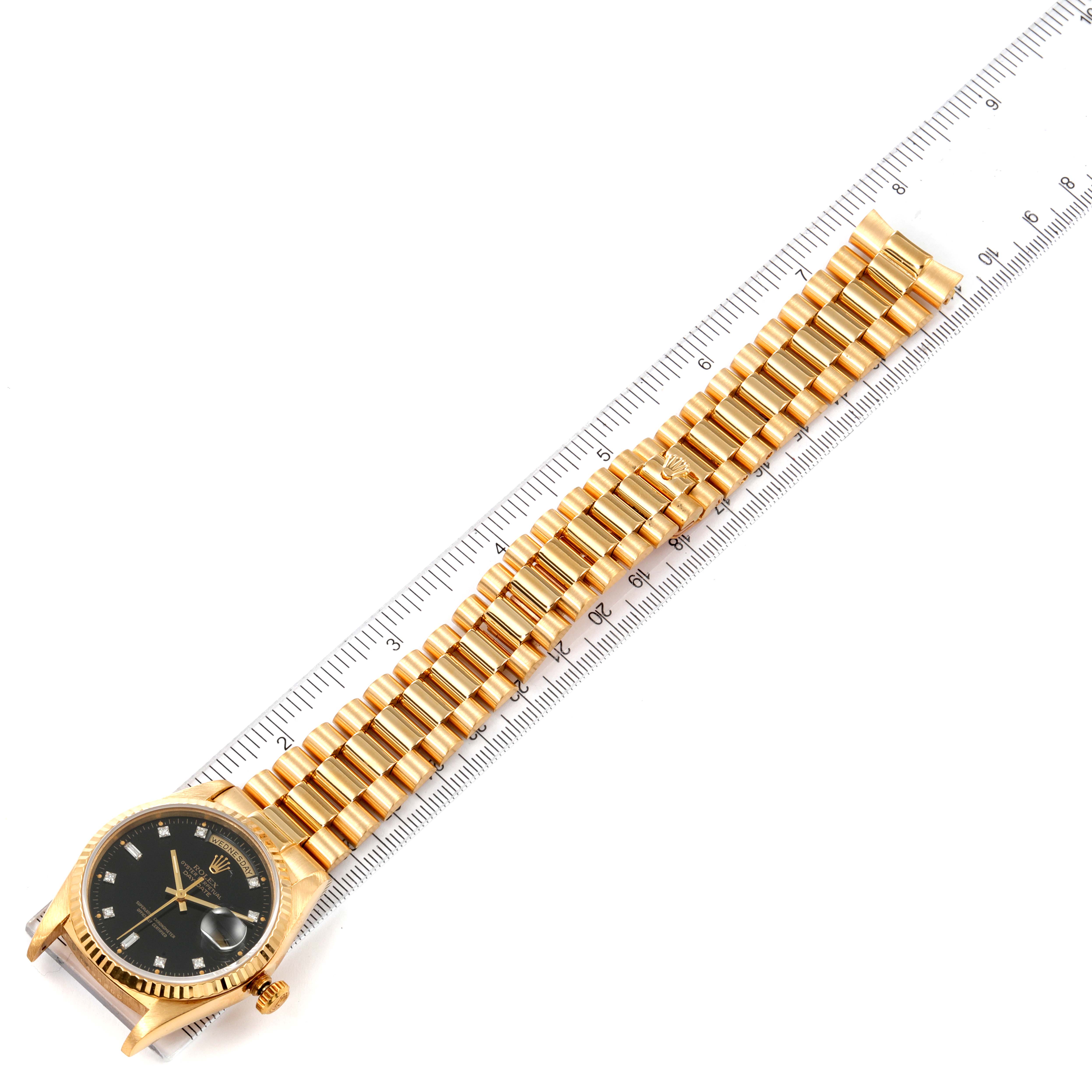 The image shows a Rolex President 18238 Men's Yellow Gold Black Dial 18238 Men's Yellow Gold Black Dial watch laid flat next to a ruler, highlighting its strap and face.