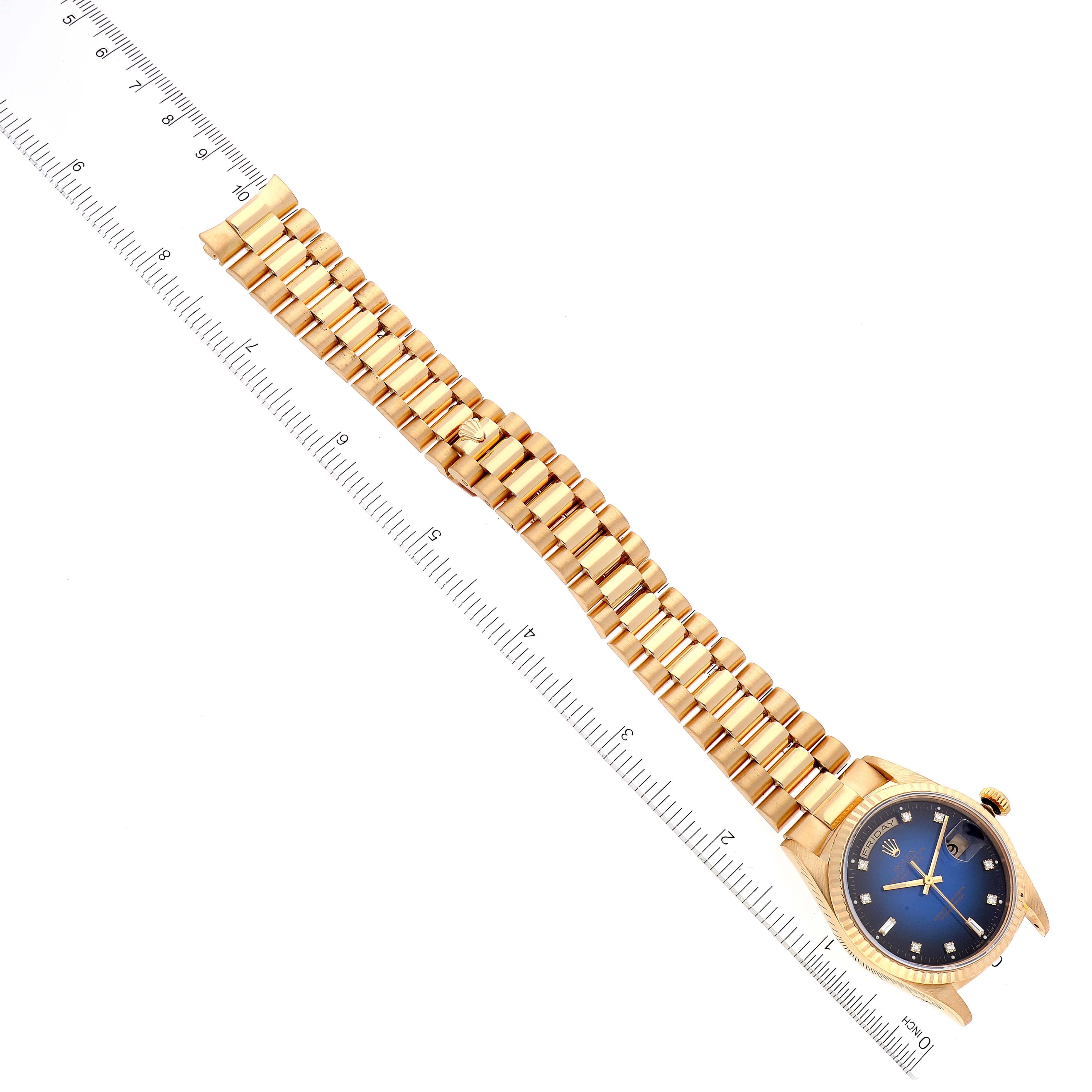 This image shows a Rolex President 18238 Men
s Yellow Gold Blue Dial 18238 Men
s Yellow Gold Blue Dial model watch, highlighting its gold bracelet and blue dial, laid next to a ruler.