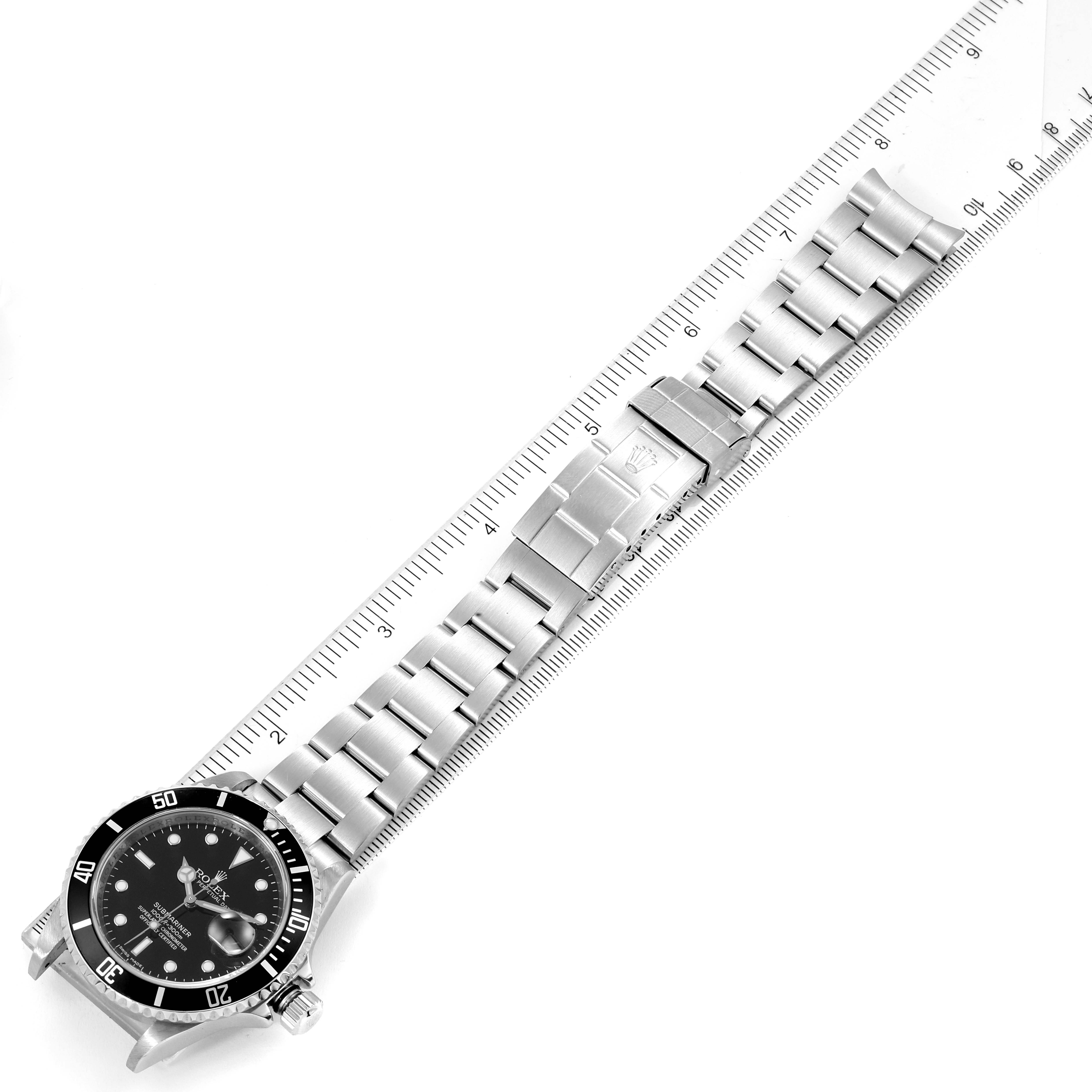The image shows the entire Rolex Submariner 16610 Men
s Stainless Steel Black Dial 16610 Men
s Stainless Steel Black Dial watch including the face, bezel, and bracelet laid next to a ruler for measurement.
