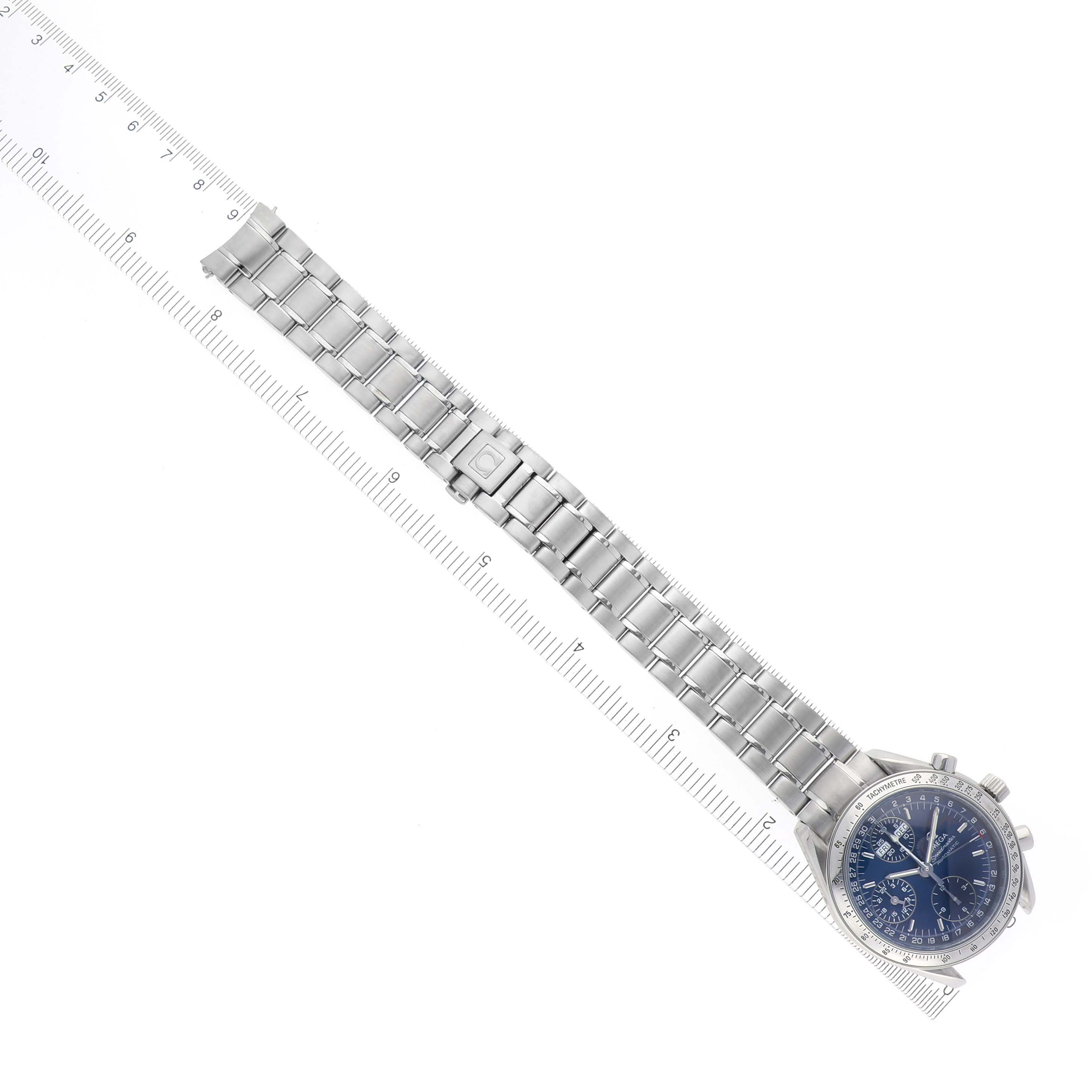 The Omega Speedmaster 3523.80.00 Men
s Stainless Steel Blue Dial 3523.80.00 Men
s Stainless Steel Blue Dial watch is shown from an overhead angle, displaying its full bracelet and the watch face next to a ruler.