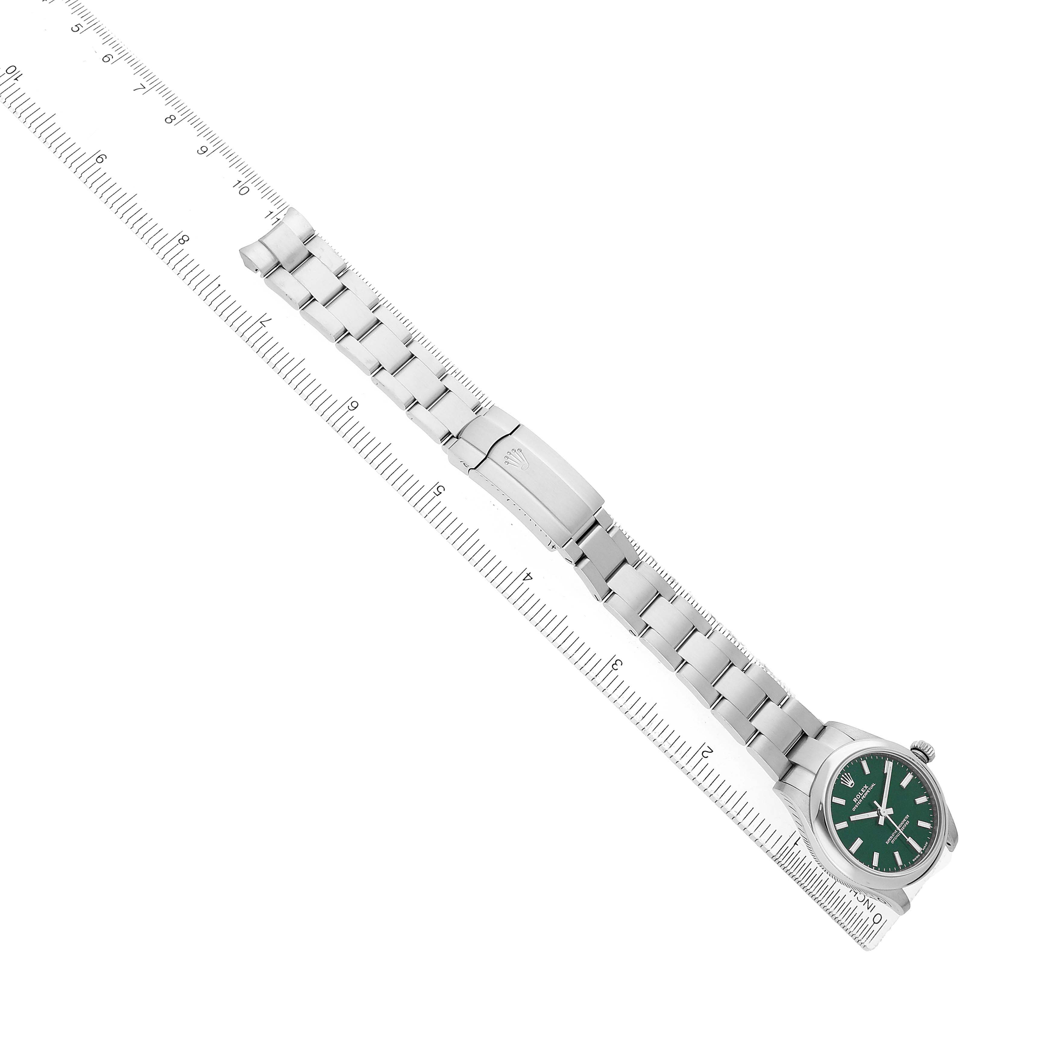 The Rolex Mid-Size 277200 Women's Stainless Steel Green Dial watch is shown from a top-down angle, displaying the face, bracelet, and clasp alongside a ruler for scale.