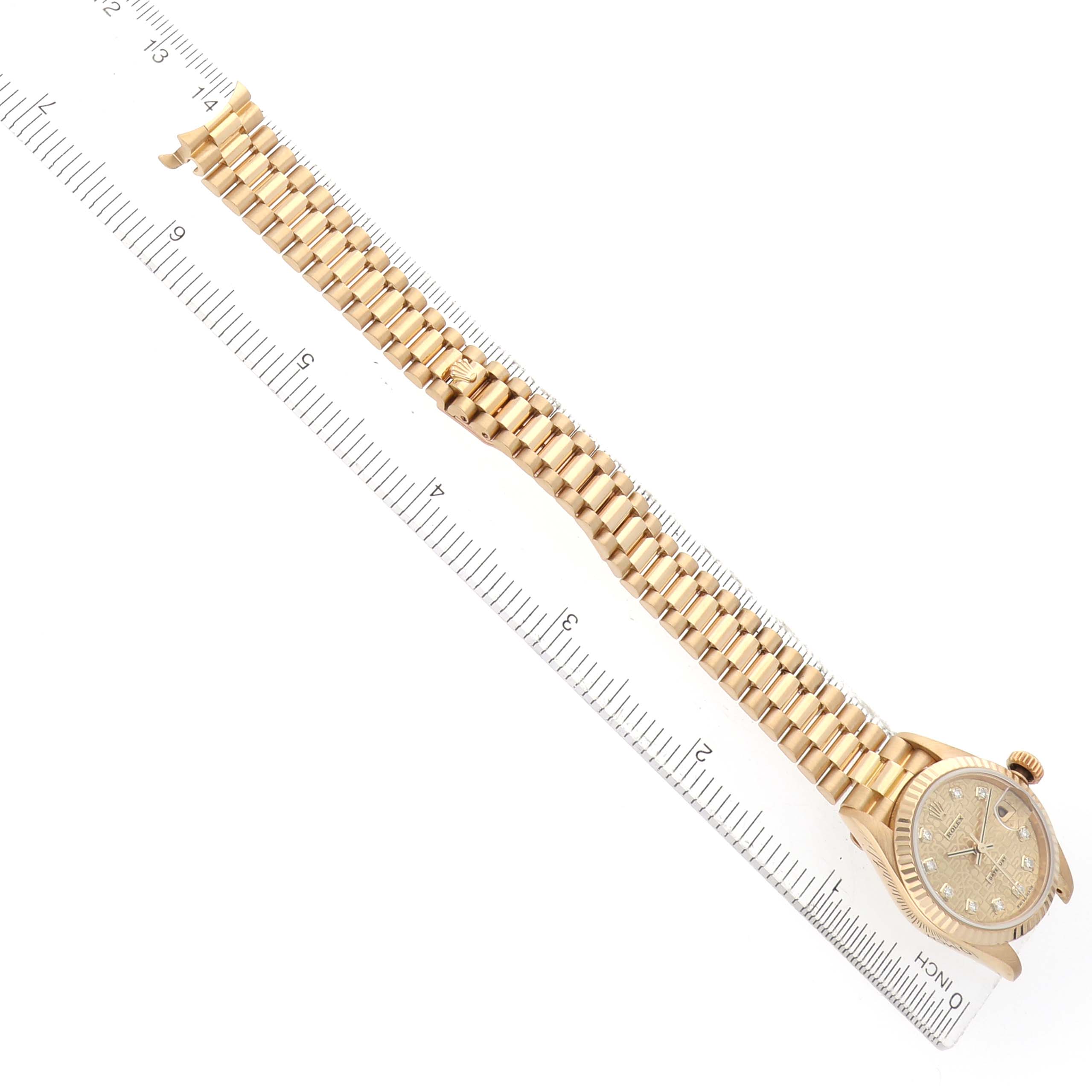 The image shows the Rolex President 179178 Women's Yellow Gold Champagne Dial watch laid flat with a gold strap and diamond markers, viewed from a top-down angle alongside a ruler.