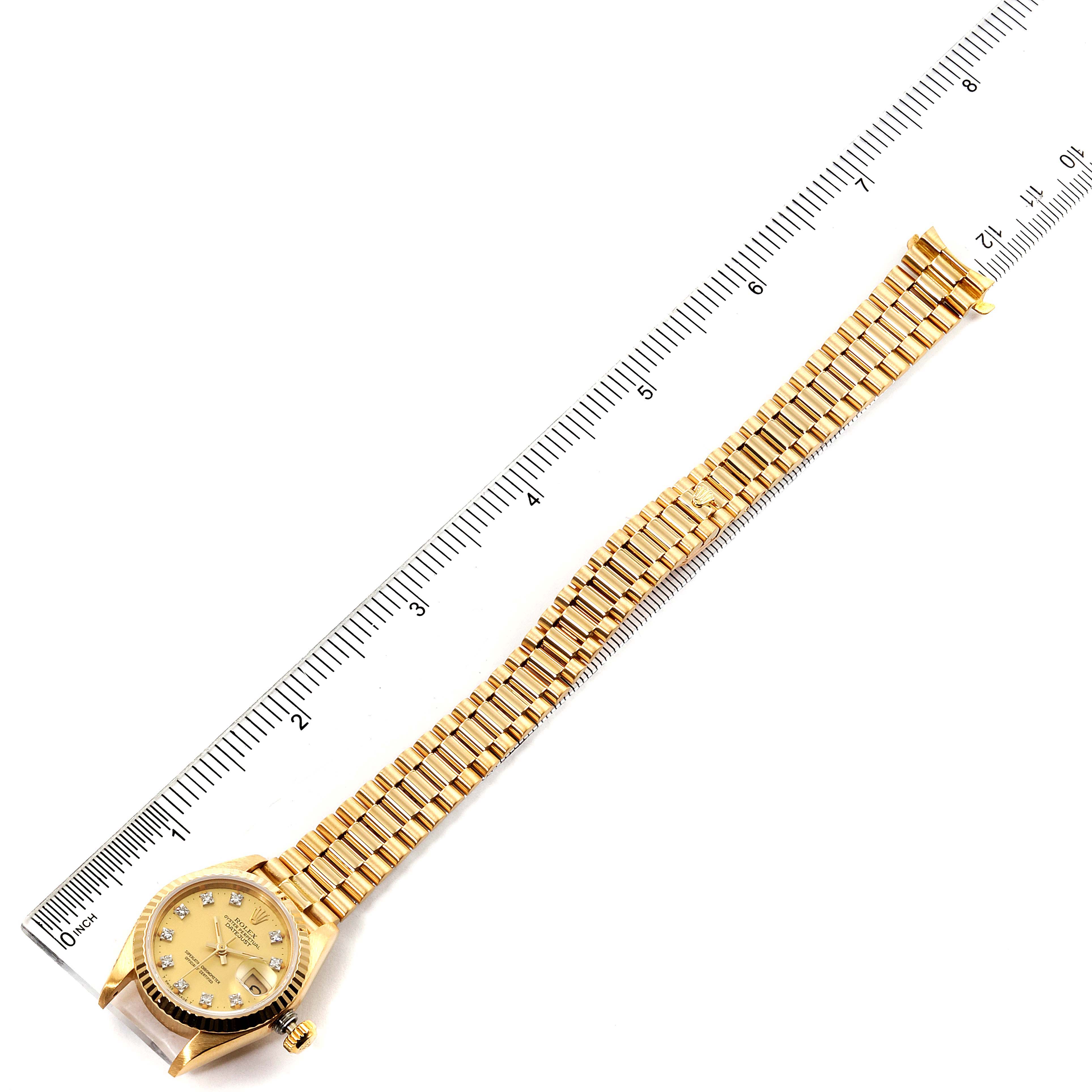 The image shows a Rolex President 69178 Women
s Yellow Gold Champagne Dial 69178 Women
s Yellow Gold Champagne Dial model watch laid flat next to a ruler, displaying the watch face and full bracelet.