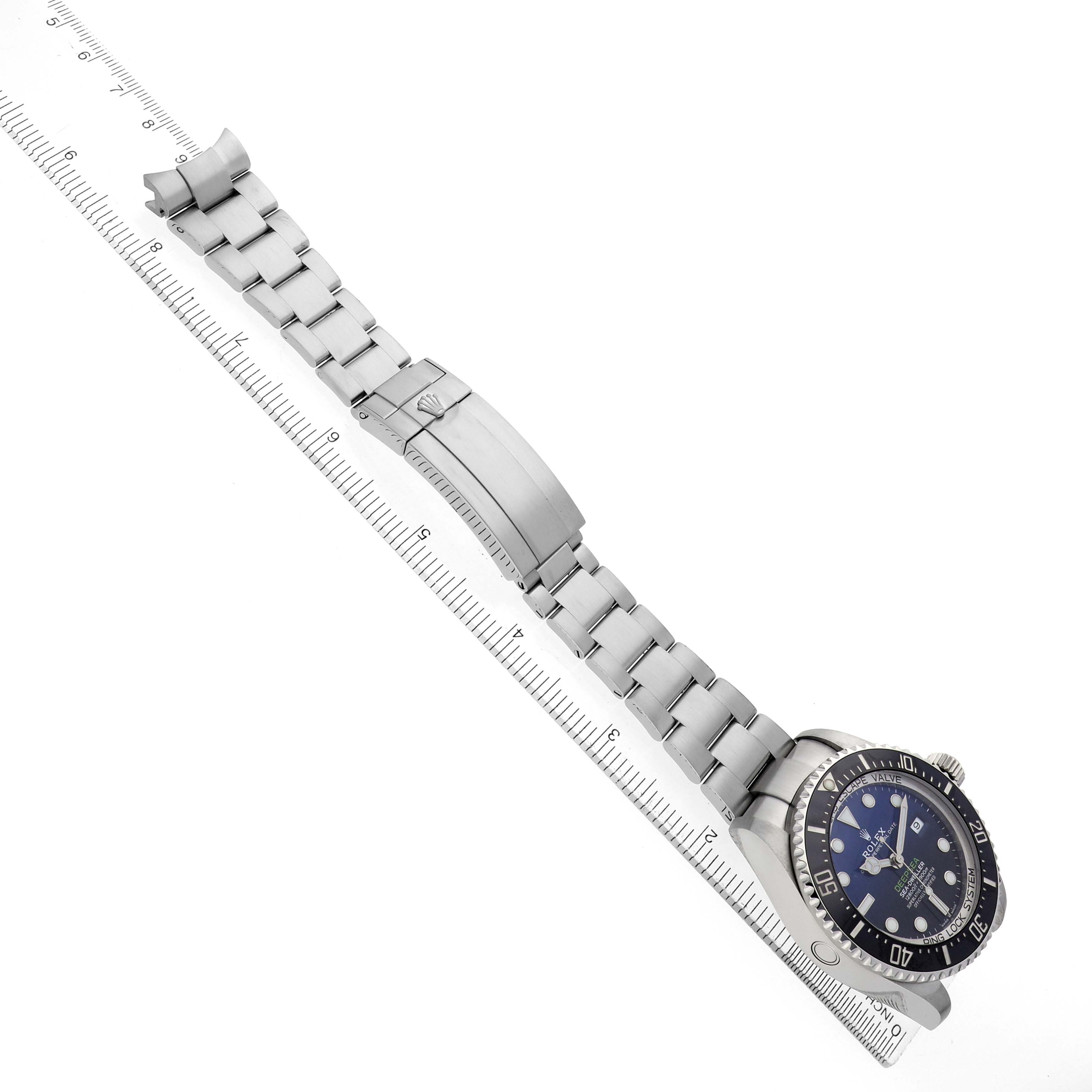 The Rolex Sea-Dweller 126660 Men's Stainless Steel Blue Dial watch is shown at an angle displaying its face, bezel, and bracelet, laid alongside a ruler.