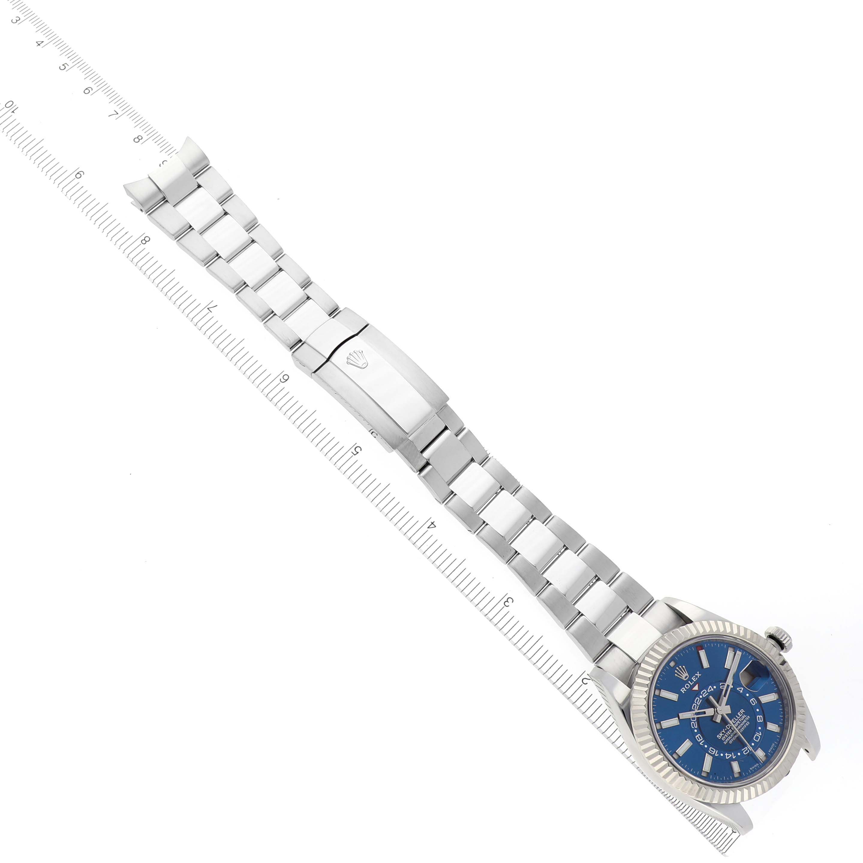The image shows a Rolex Sky-Dweller 326934 Men
s Stainless Steel Blue Dial 326934 Men
s Stainless Steel Blue Dial watch at a slight angle, displaying the blue dial, bezel, and full bracelet alongside a ruler.