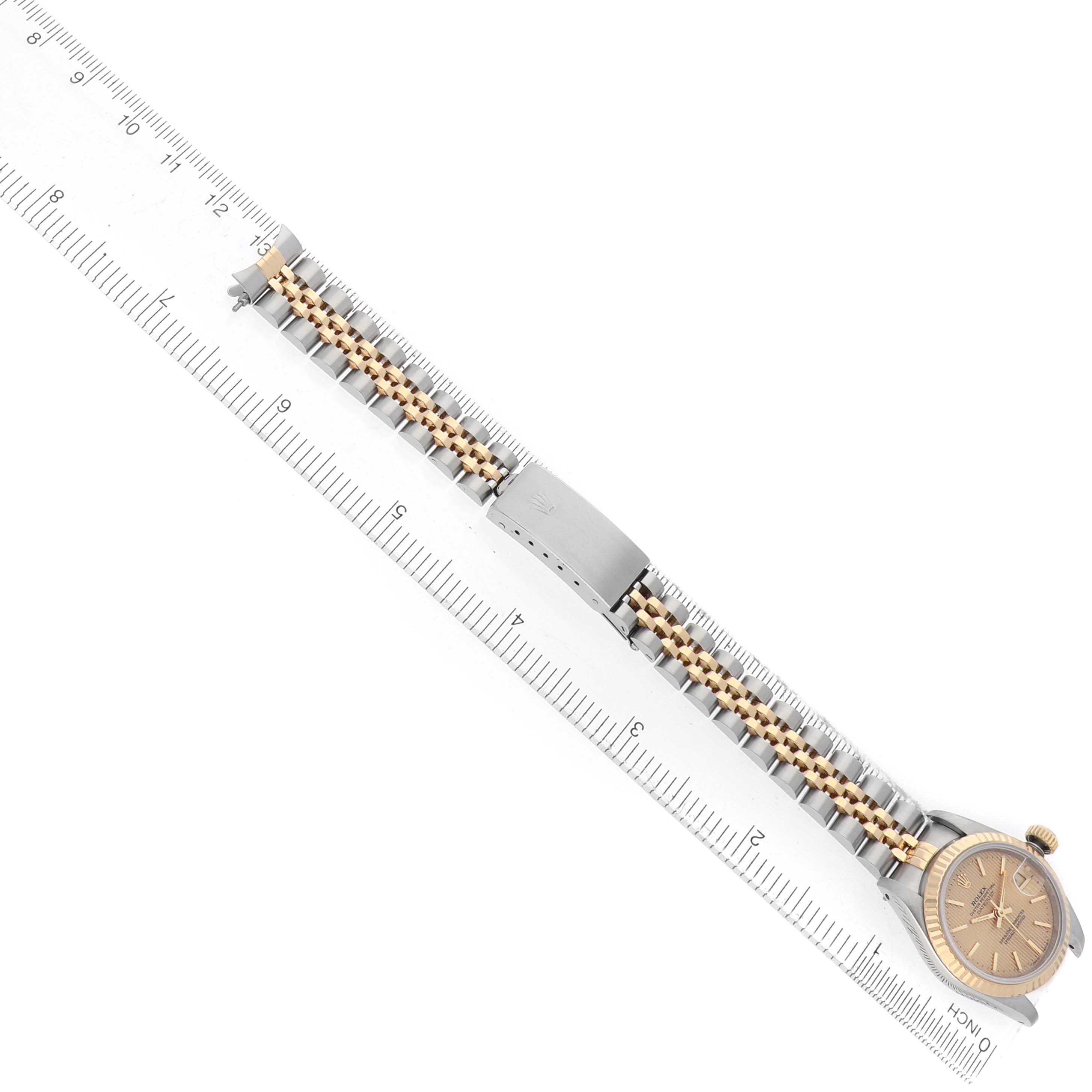 The Rolex Datejust 69173 Women's Steel and Gold (two tone) Champagne Dial watch is shown in a full-length side angle, displaying the bracelet, clasp, and face alongside a ruler for scale.