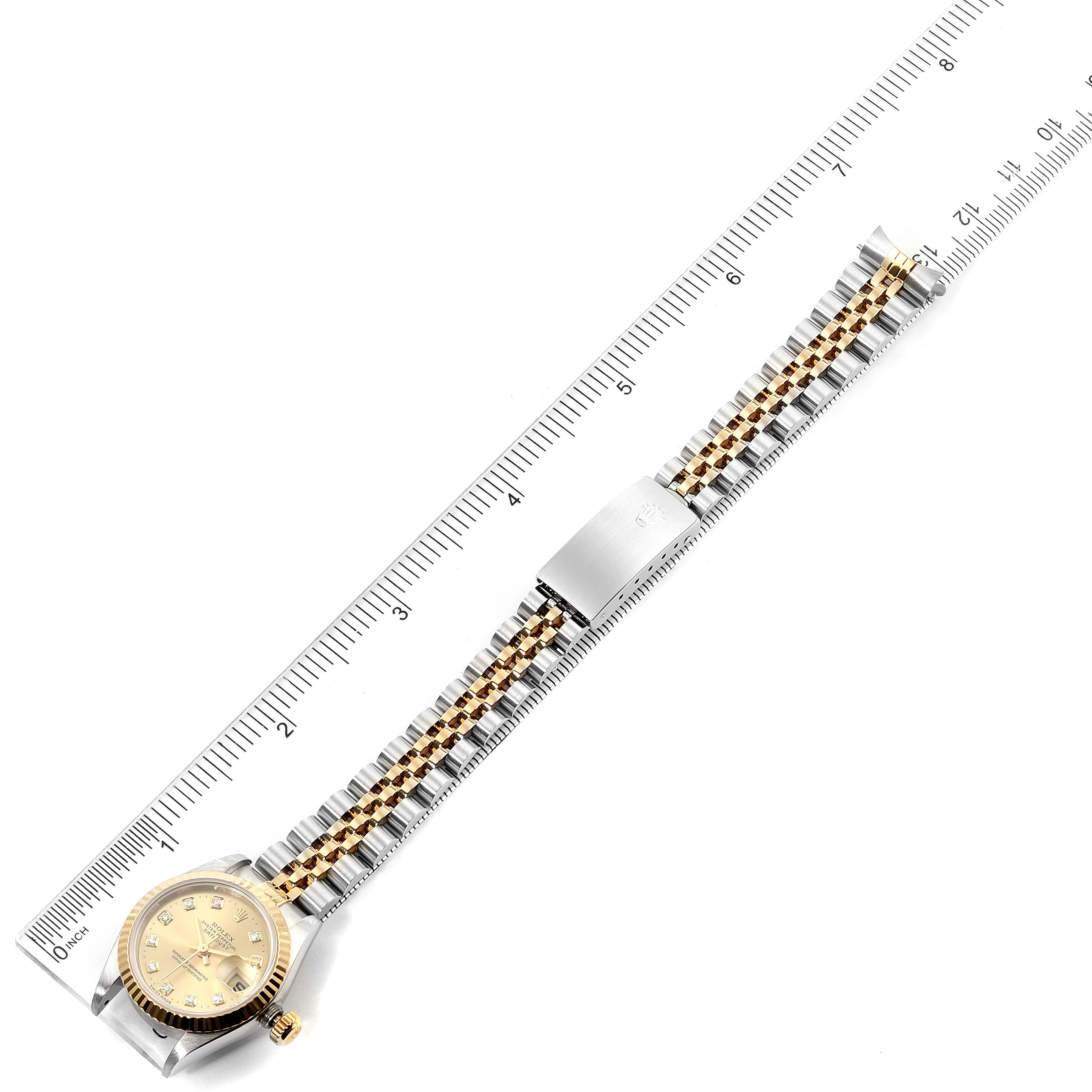 The image displays a full view of the Rolex Datejust 69173 Women
s Steel and Gold (two tone) Champagne Dial 69173 Women
s Steel and Gold (two tone) Champagne Dial watch placed alongside a ruler, showing its bracelet, clasp, and dial.